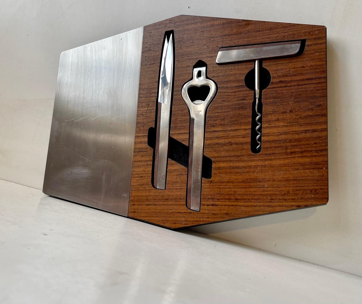 A cool a set of bar accessories that comes integrated into a stylish cutting board in stainless steel and teak. They accessories are: lime/cheese knife, bottle opener and a corkscrew also fashioned from teak and stainless. This set was made in