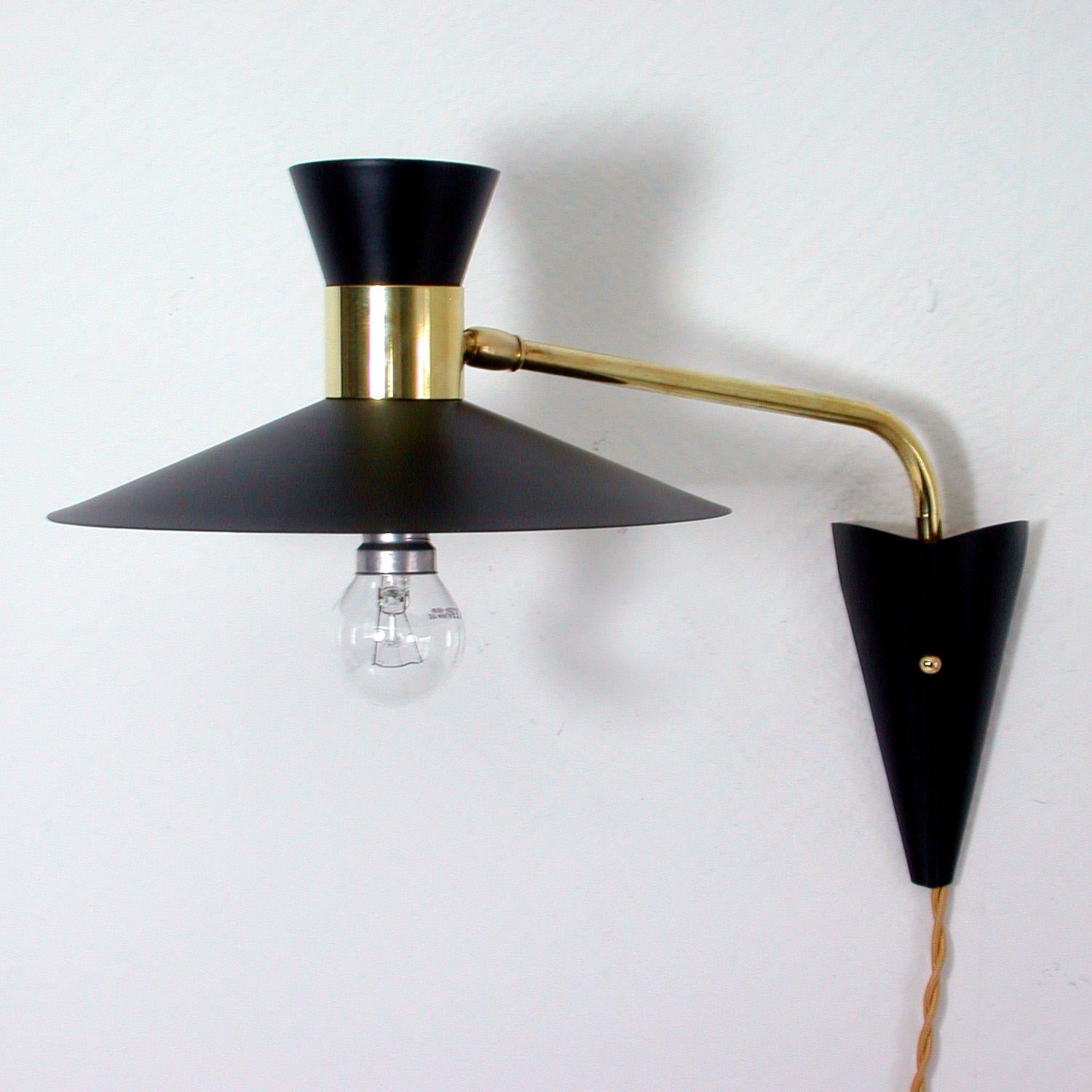 This 1950s articulating wall lamp was designed and manufactured in France.

The wall light has got a black diabolo-shaped lampshade and brass swiveling lamp arm with brass details and a black lacquered wall fixture. The lamp has been rewired and