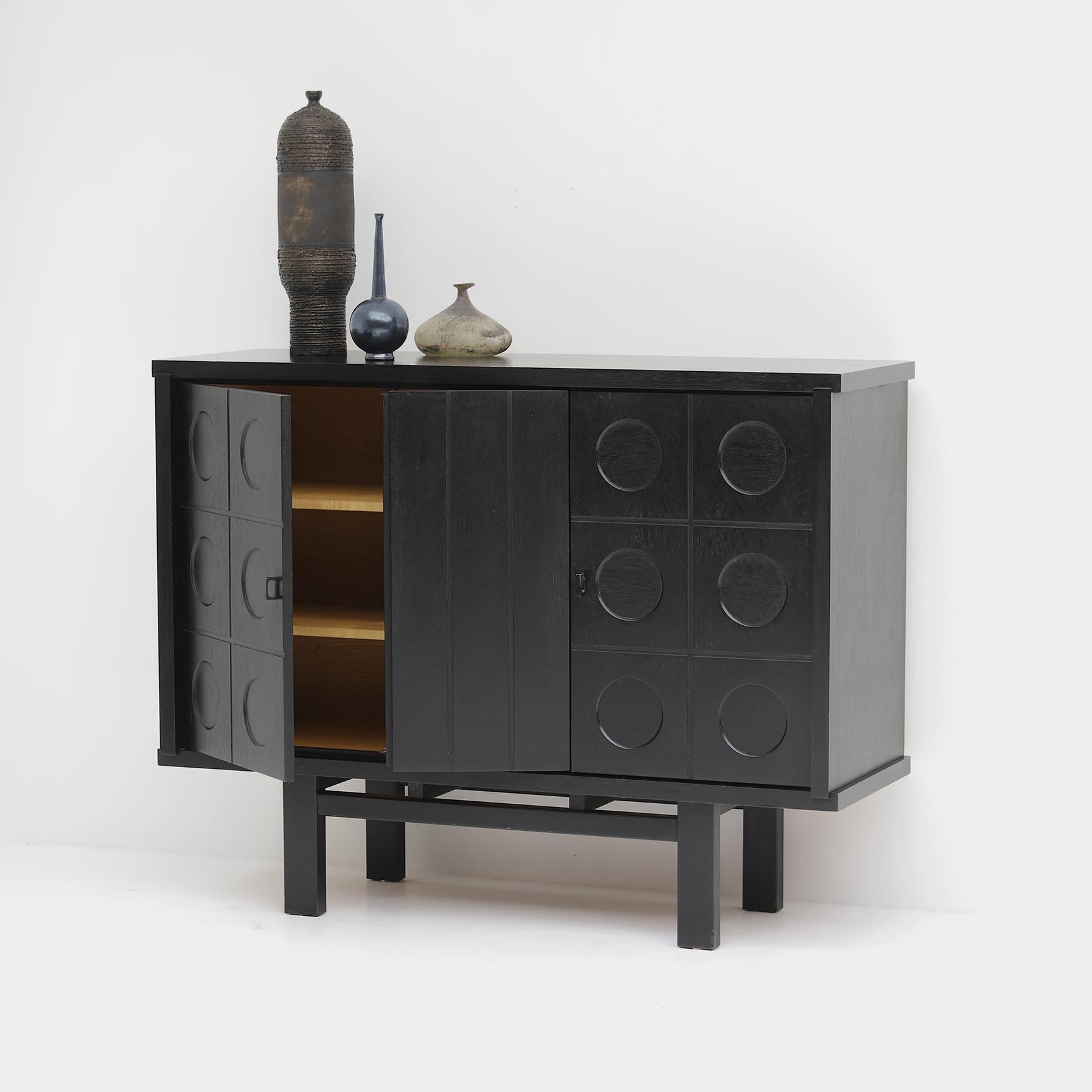 A timeless piece of brutalist craftsmanship from the 1970s, manufactured in Belgium. The cabinet is made out of a black ebonized oak and had metal doorhandles. It features two graphic patterned doors that provides plenty of storage which makes it