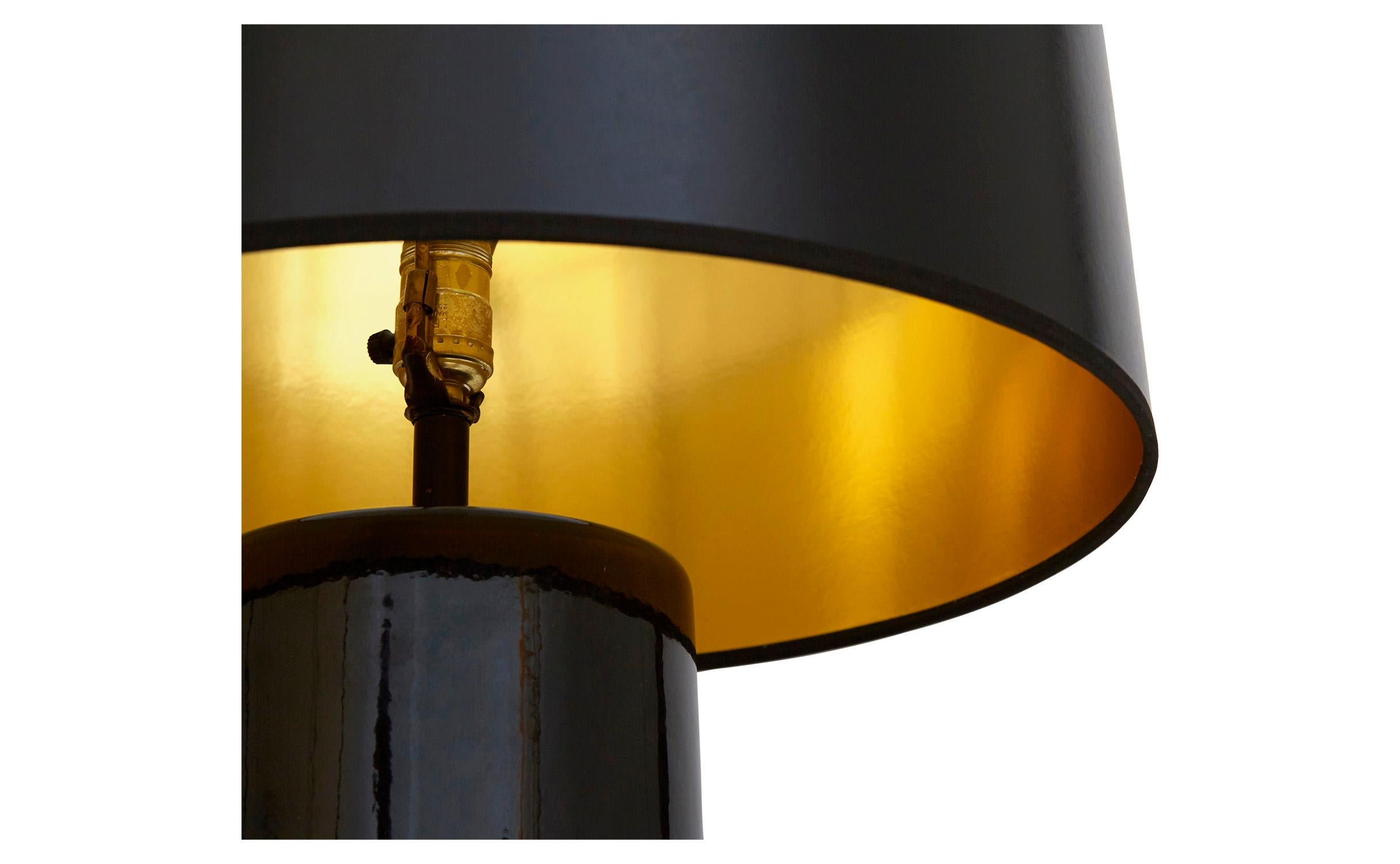 Our vintage black table lamp was crafted in America in the mid-20th century. It features a cylindrical ceramic base finished with a glossy black glaze and paired with a black paper shade with a gold interior. Newly rewired, we’ve paired it with a