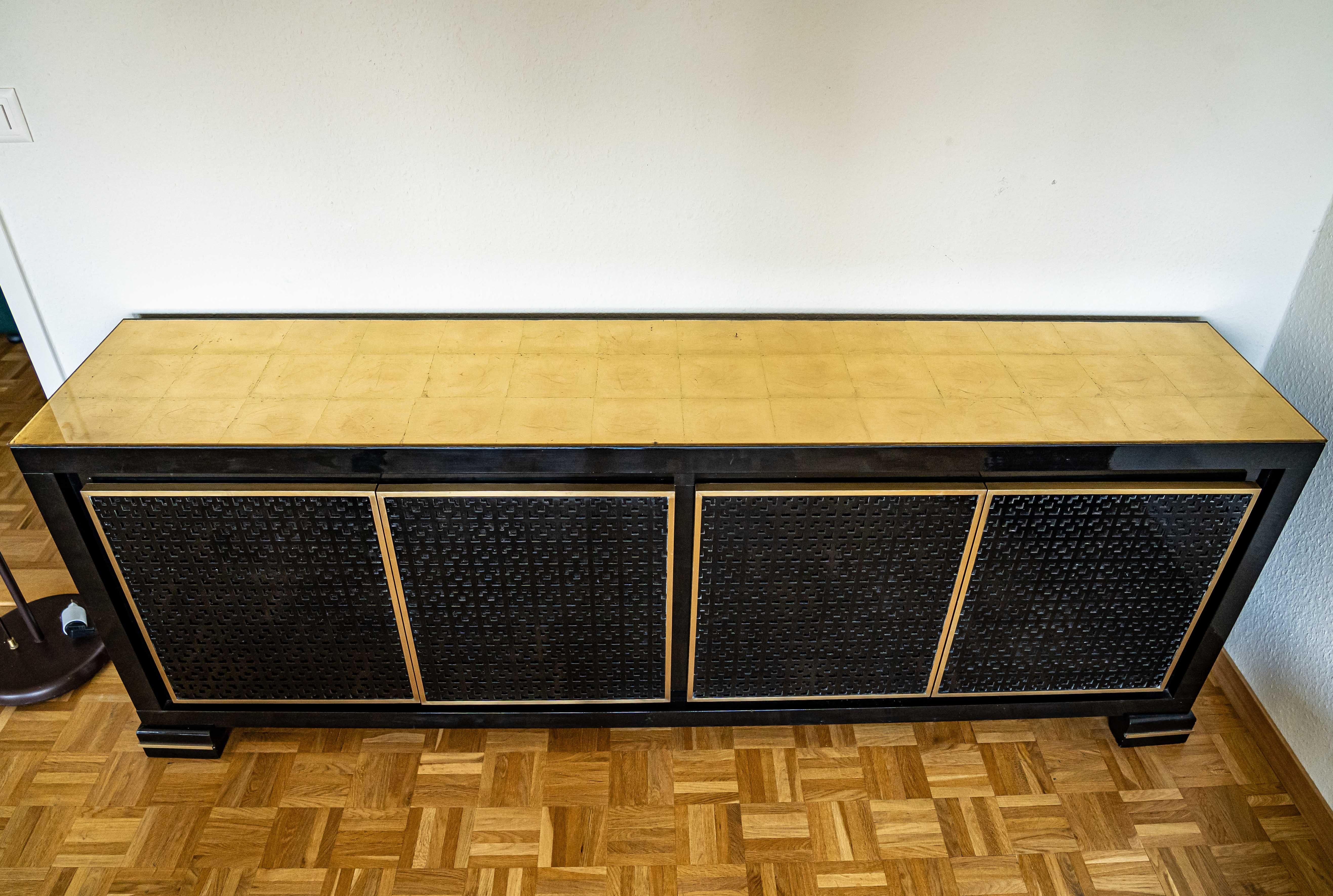 Midcentury black lacquered credenza with a sets of drawers and shelves, red lacquered inside.
Gold leaf glass top.