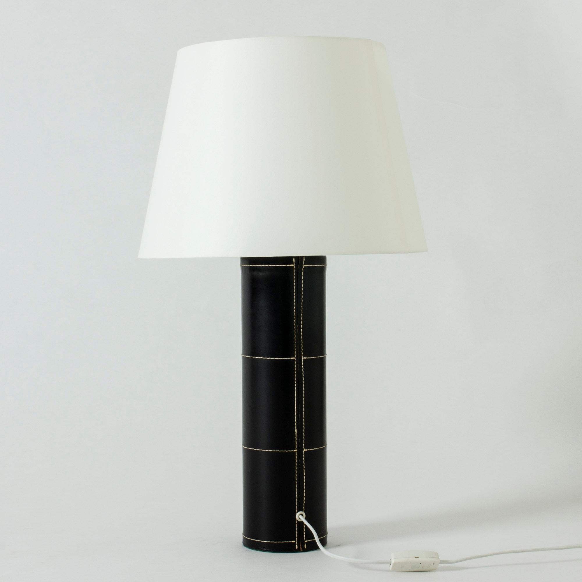 Large table lamp from Bergboms with a cylinder base dressed in black leather. Decorated with white seams – a Minimalist design with a deluxe finish.