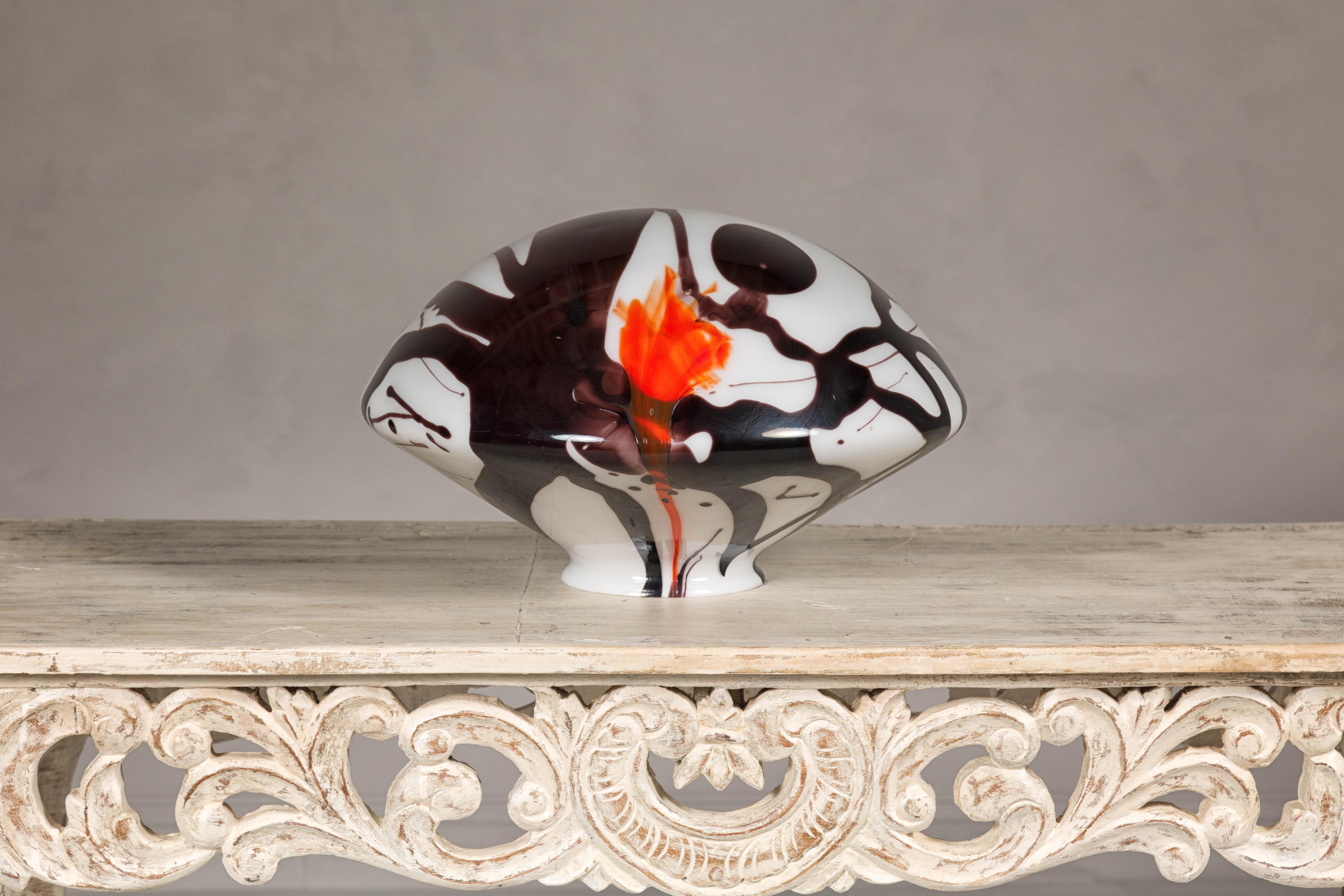 A Midcentury blown glass dome with black, white and orange abstract décor. This midcentury blown glass dome captivates with its swirling abstract décor, where black, white, and vibrant orange hues dance together in a harmonious blend of color and