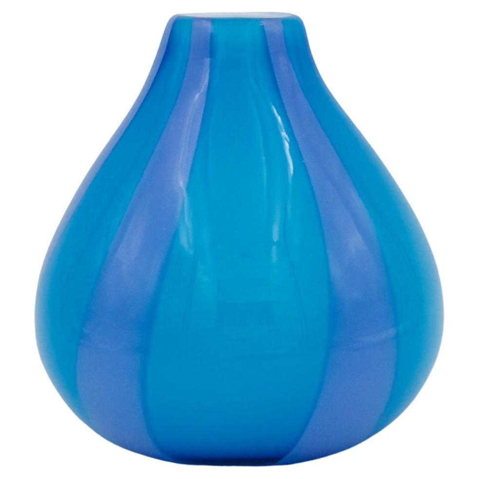 A substantial and colorful handmade cased glass vase in a bold sky blue with contrasting stripes of lavender with a white interior. The colorful striped art glass design is called 