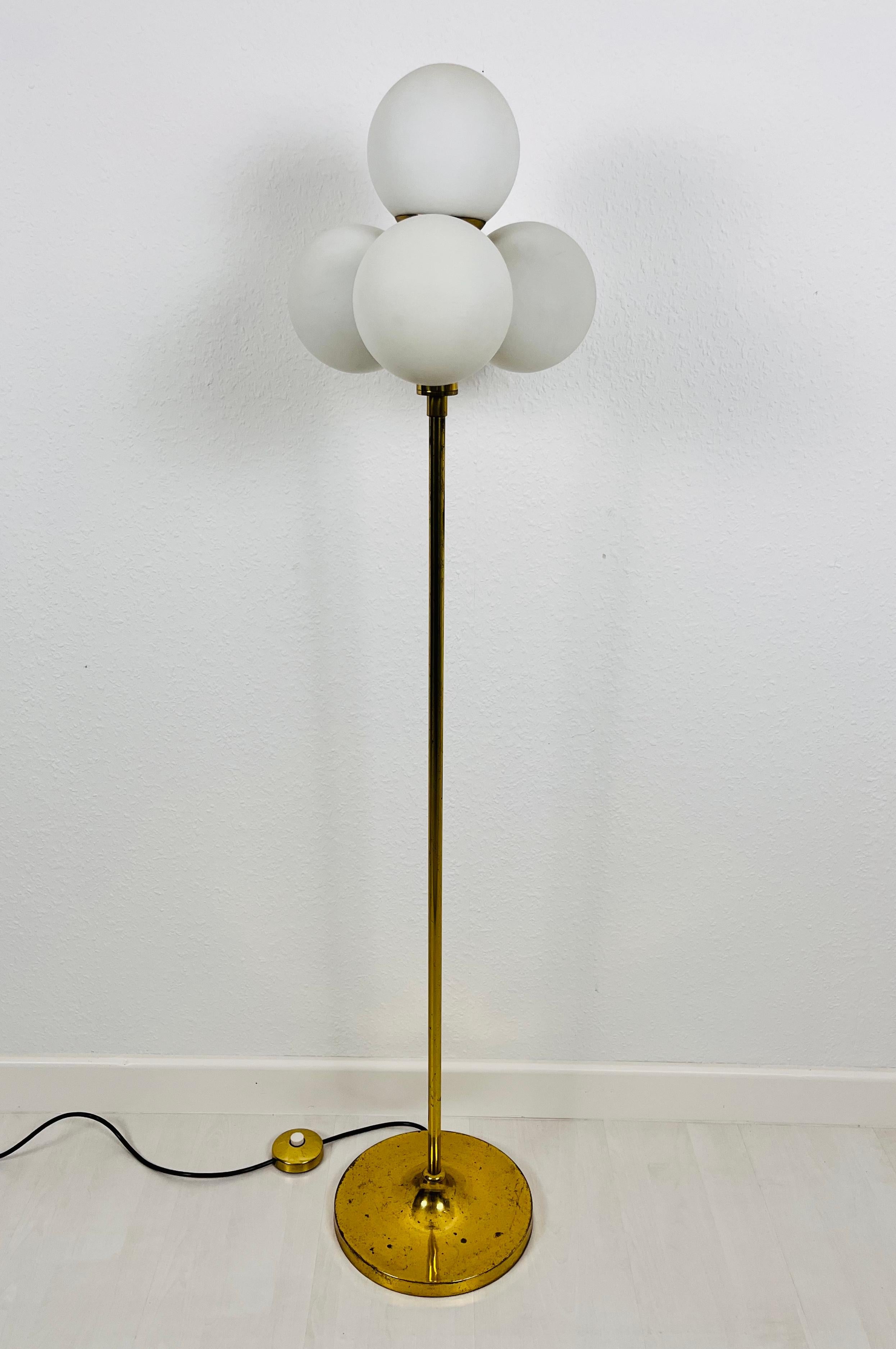 A midcentury floor lamp by Kaiser made in Germany in the 1960s. It is fascinating with its Space Age design and four ball shaped opaque balls. The bottom of the light is made of full brass. The bar is also made of brass including the arms.

Very