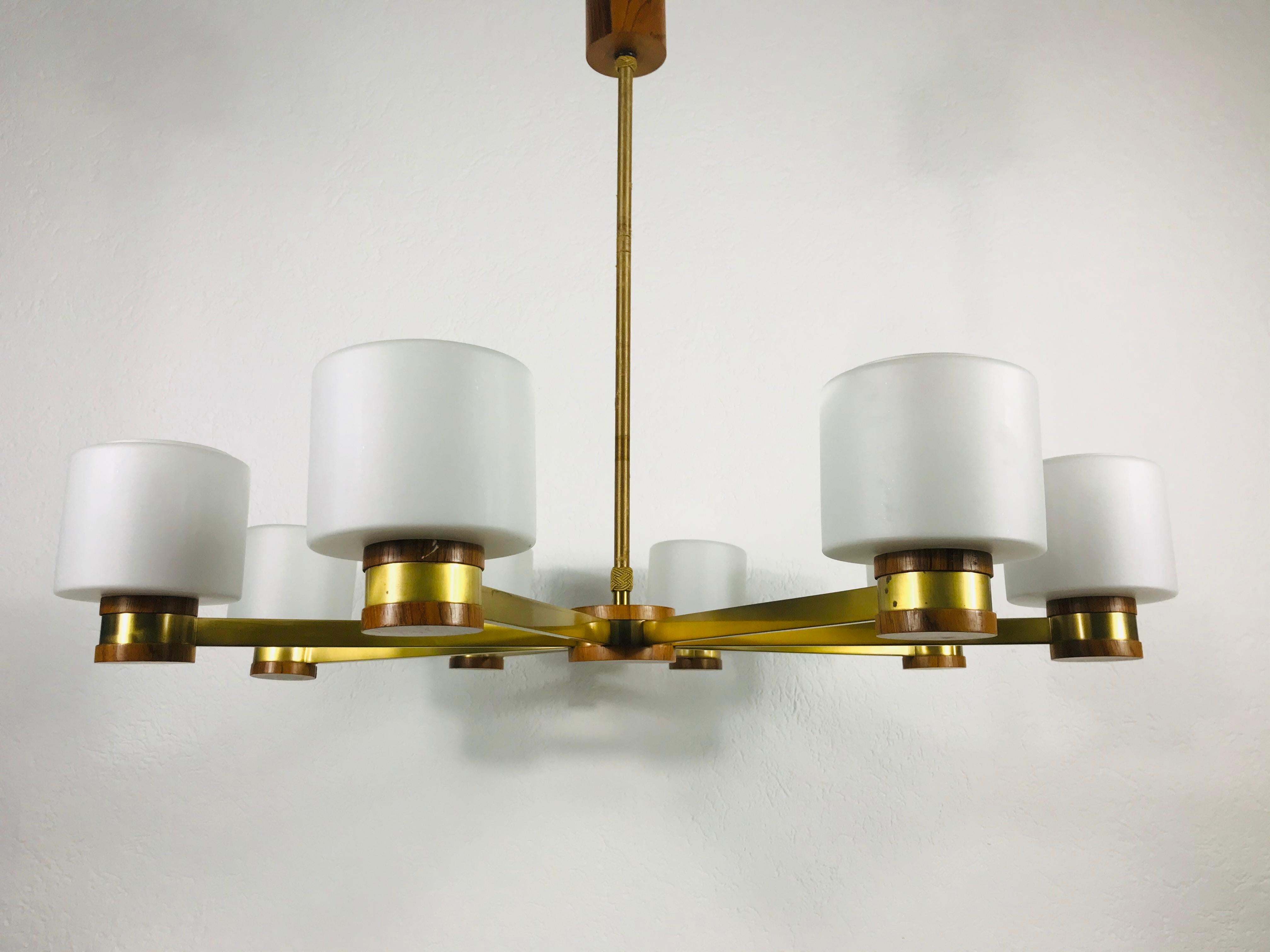 Mid-Century Modern chandelier made in the 1960s. It has eight brass arms, each with an opaline glass shade. The top and the bottom of the rope bar and the bottom of the glass shades are made of wood.

The light requires eight E27 light bulbs.