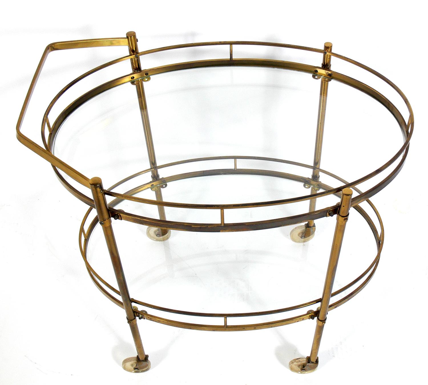 Midcentury brass bar cart, probably Italian, circa 1960s. Two large oval glass shelves provide lots of storage. Can be used as a bar cart, serving cart, or as movable storage in an office. Retains warm original patina.