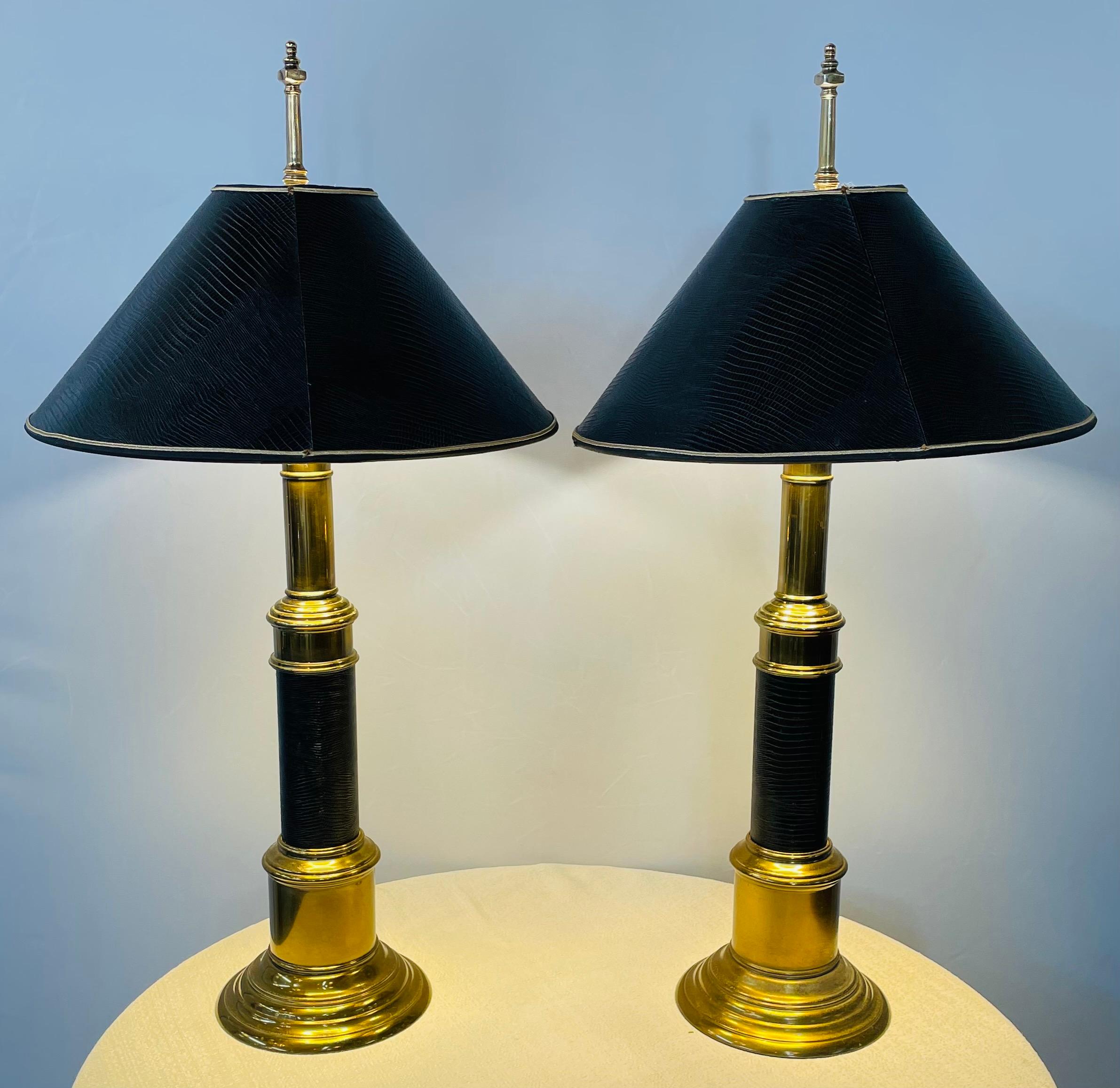A Mid-Century Modern pair of elegant table lamps attributed to Stiffel. Each lamp is made of heavy solid brass with the column wrapped in black embossed leather matching its original bell shades. Elegant, classy and very stylish, the pair of lamps