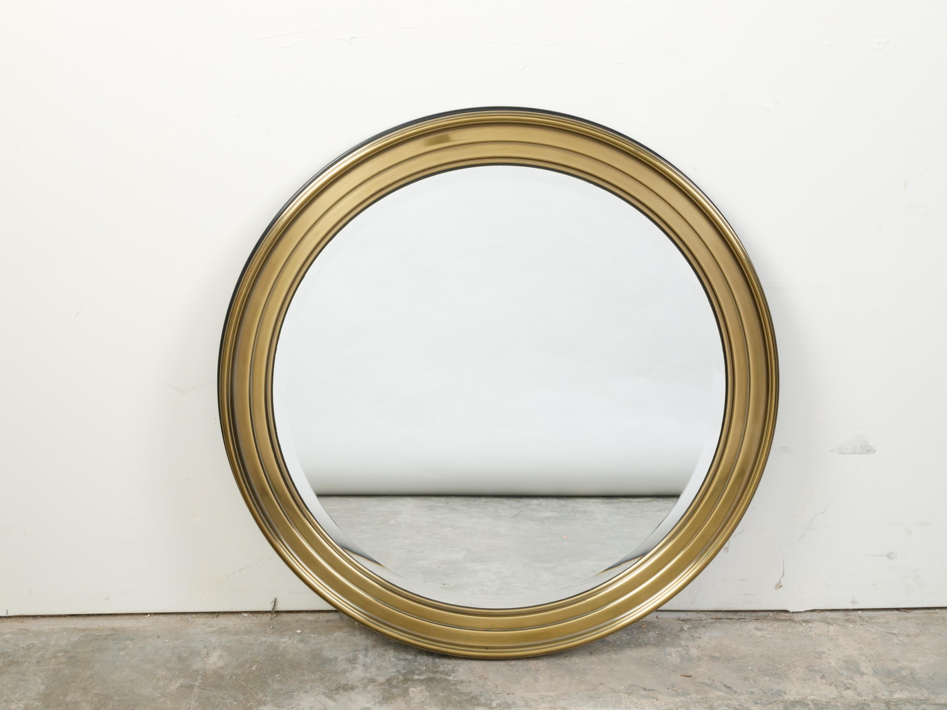 A French vintage brass round mirror from the mid 20th century, with beveled accents. Created in France during the midcentury period, this brass mirror features a circular frame with stepped accents, surrounding a mirror plate with beveled edge. With