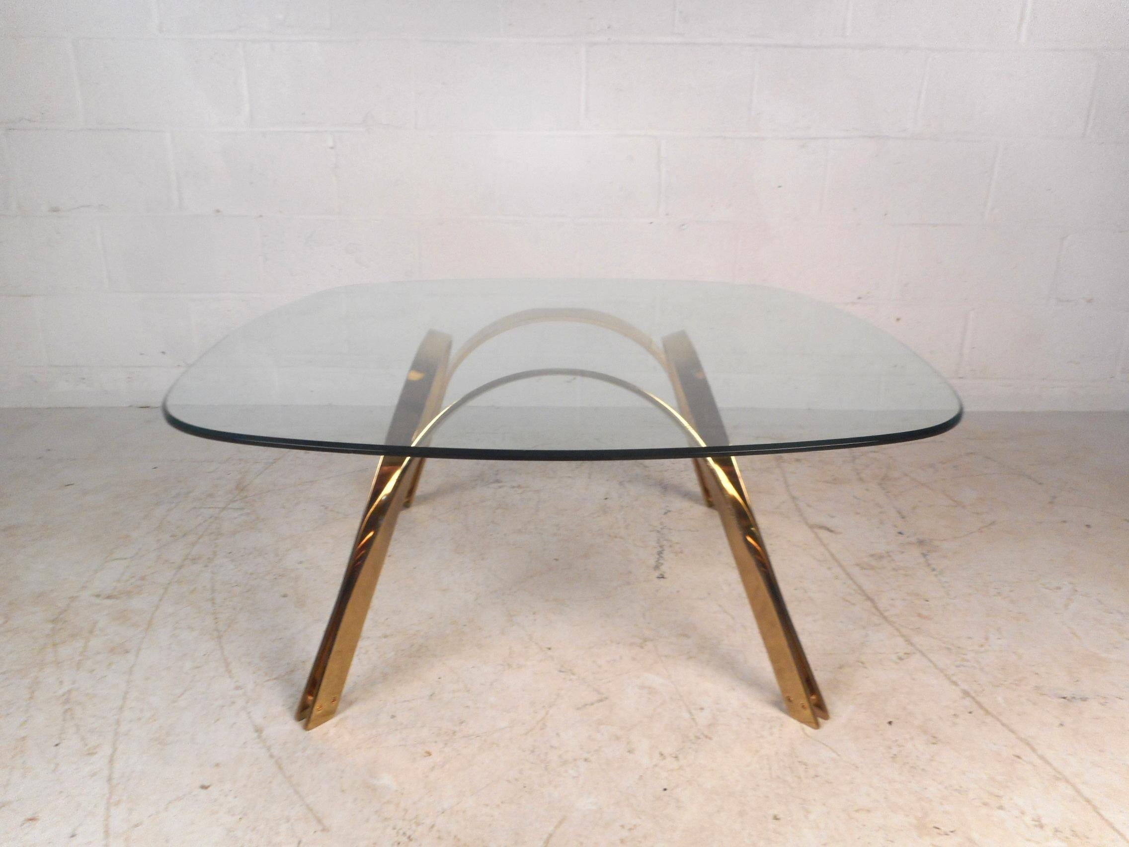 This stunning coffee table from the 1960s features a sculpted brass base with curved legs. A thick glass top with rounded edges and a solid flat bar base shows true quality. This stylish midcentury piece makes the perfect addition to any modern