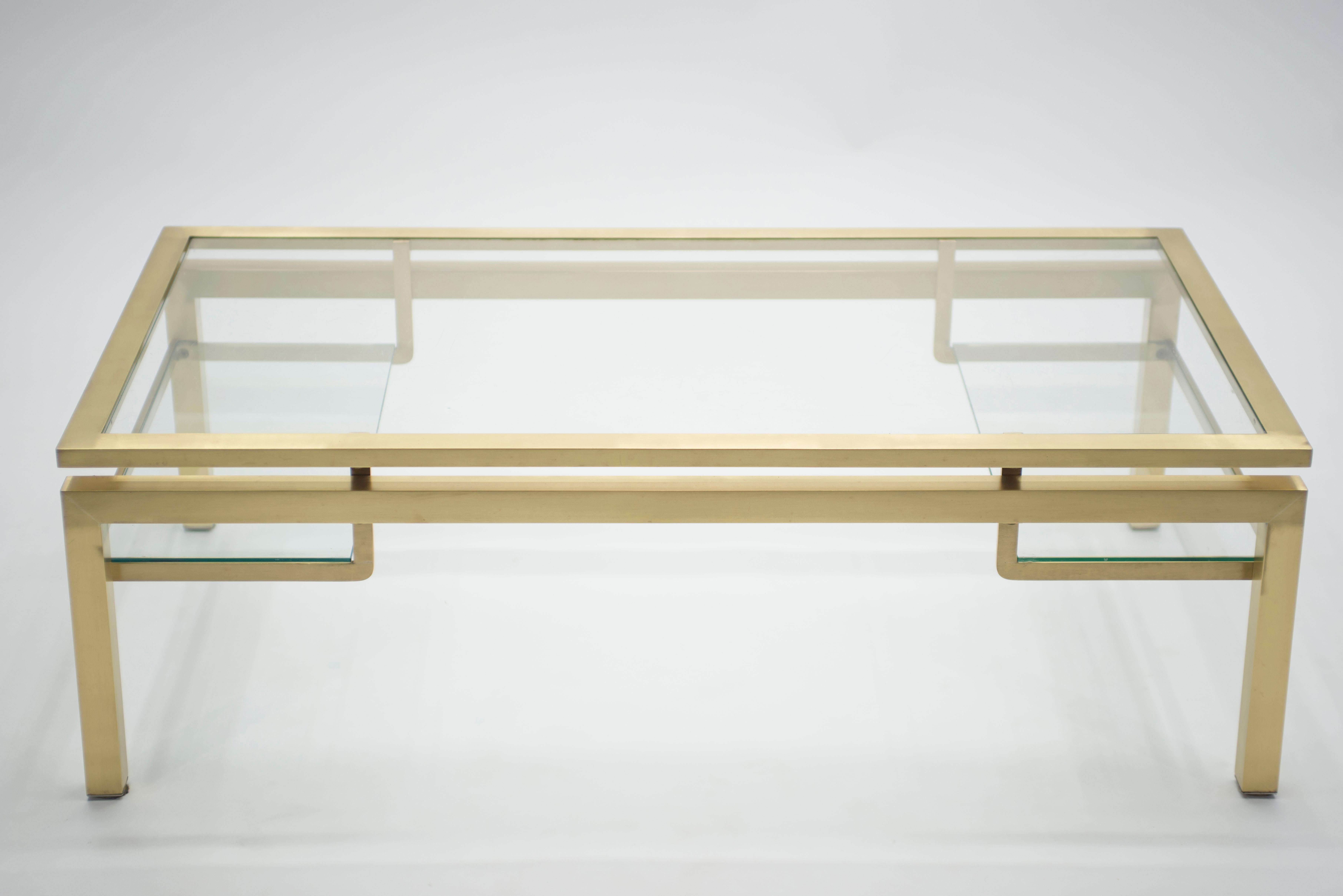 Simple lines point to this coffee table’s midcentury roots. Designed by Guy Lefevre for Maison Jansen, it features silky brass legs, two small glass shelves and a glass top. Its symmetry, elevated glass, and Asian inspired and strong architectural