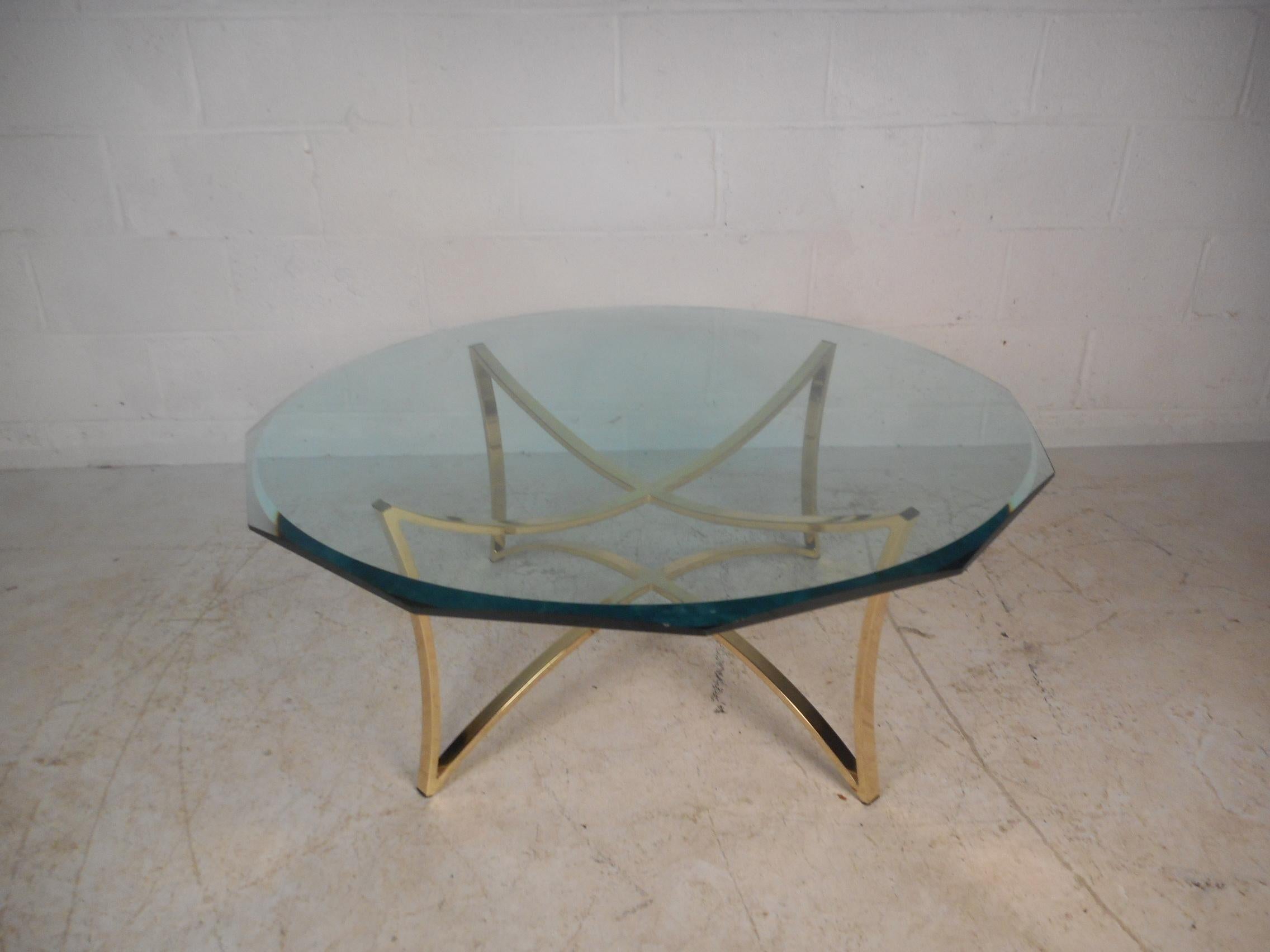 This stunning midcentury coffee table features a sculpted brass base with an unusually shaped, thick glass top. A sleek design with a four sided base with wonderful curves and detail. This stylish piece is sure to add character to any home, business