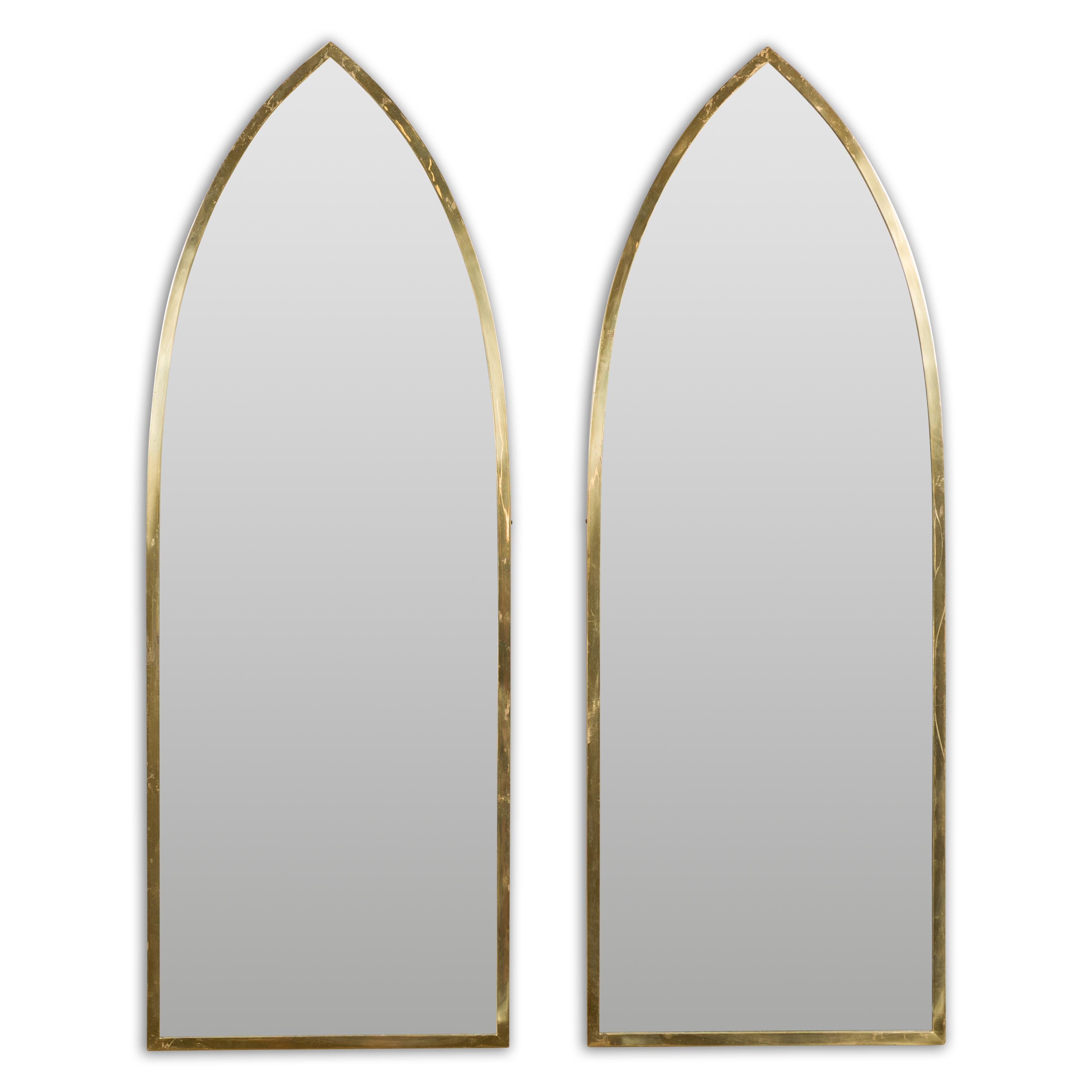 A pair of vintage Midcentury brass Gothic inspired mirrors from circa 1950 with broken arch silhouette and golden hue. Reflecting the timeless charm of the Midcentury era, this pair of vintage brass Gothic-inspired mirrors from circa 1950 resonates