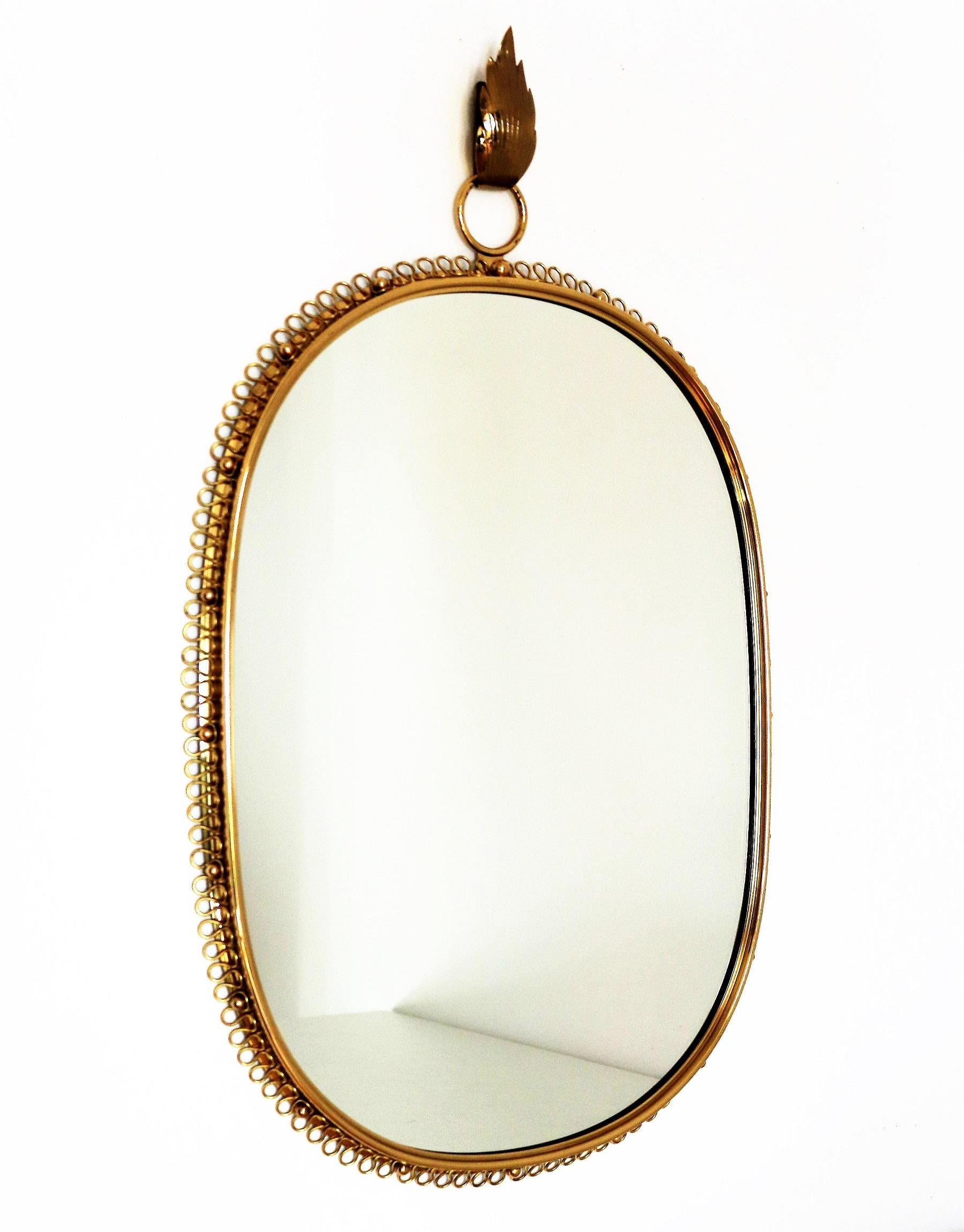 Gorgeous wall mirror designed by Austrian Josef Frank and manufactured in Sweden by Svenskt Tenn in the mid-century.
This mirror is made of full shiny brass frame with spiral loop frame around and big round hanging hook on top. 
You can easily