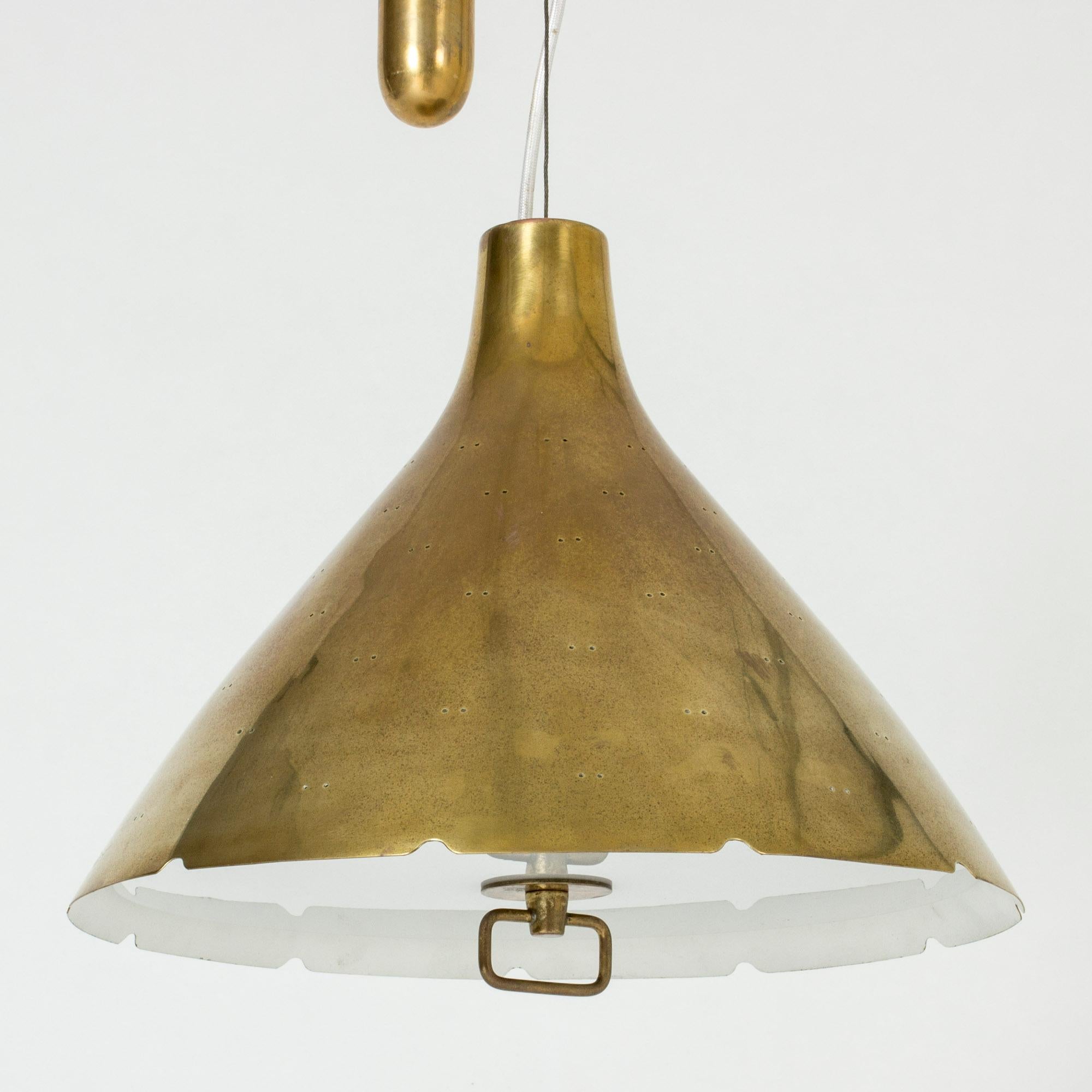 Beautiful brass ceiling lamp by Paavo Tynell, with a conical shade perforated with small holes and finished with a scalloped edge. The underside of the lamp has a glass shade that covers the light source. Decorative brass handle. Suspended with a