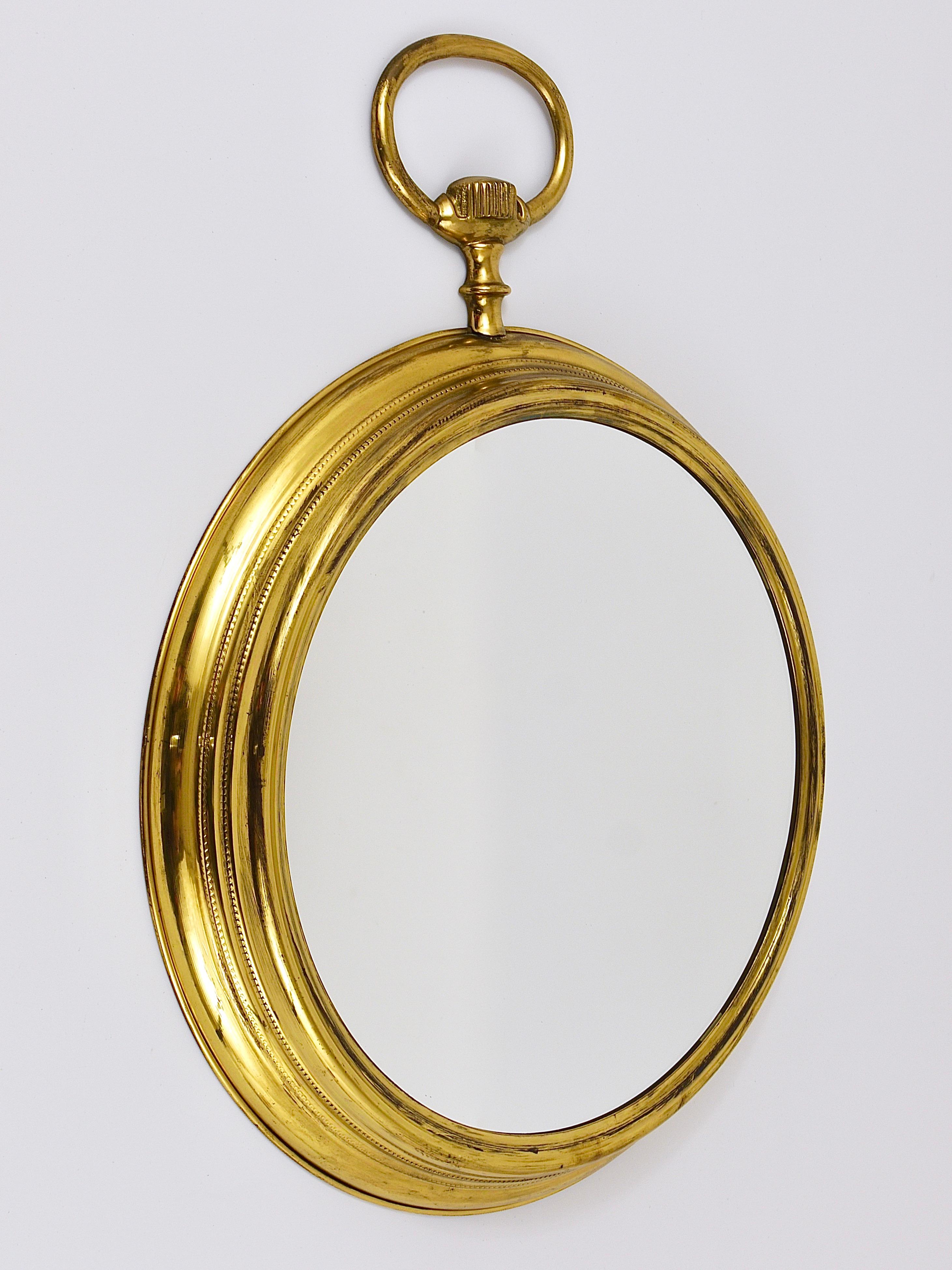 A huge 23 inches high round midcentury brass wall mirror in the shape of a pocket watch. Made in Italy in the 1950s. In the style of Piero Fornasetti. In very good original condition, with the original mirror glass and nice patina on the brass.