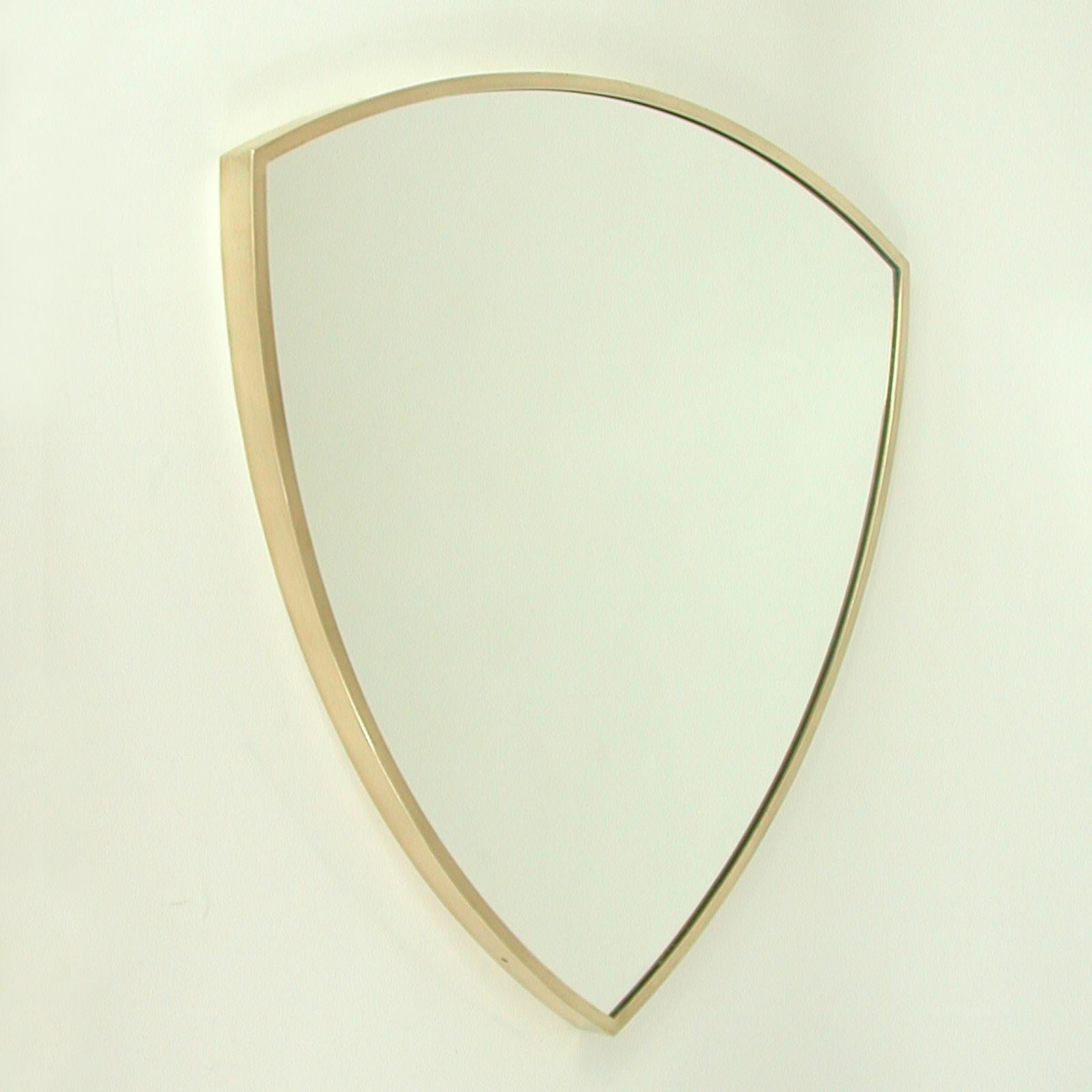 This minimalist shield shaped wall or fireplace mirror was designed and manufactured in Italy in the 1950s. It features a solid brass frame with mirror glass and wooden rear.

Very good vintage condition with few signs of use and polished frame.