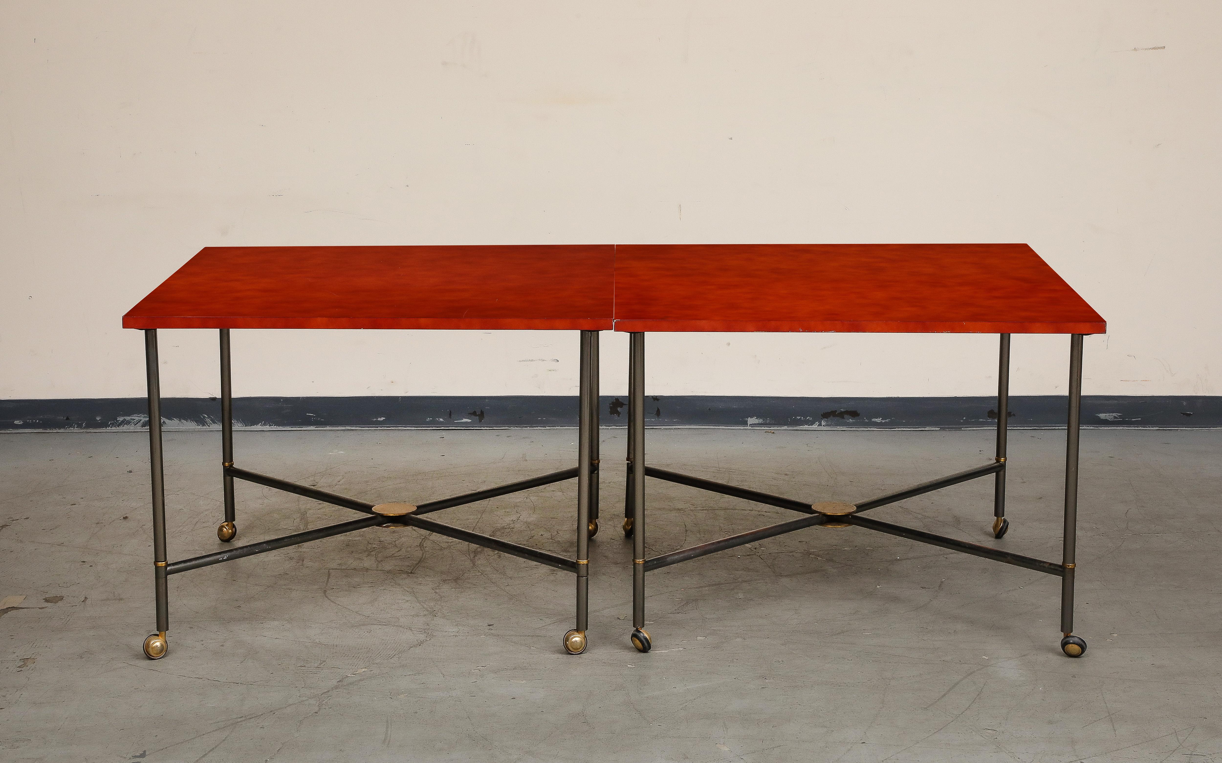 Midcentury bronze two-piece dining table on casters with red lacquer top and brass accents. Two squares join to form a longer rectangular table; there are additional pieces that could extend to an oval, however, the attachment pieces seem to be