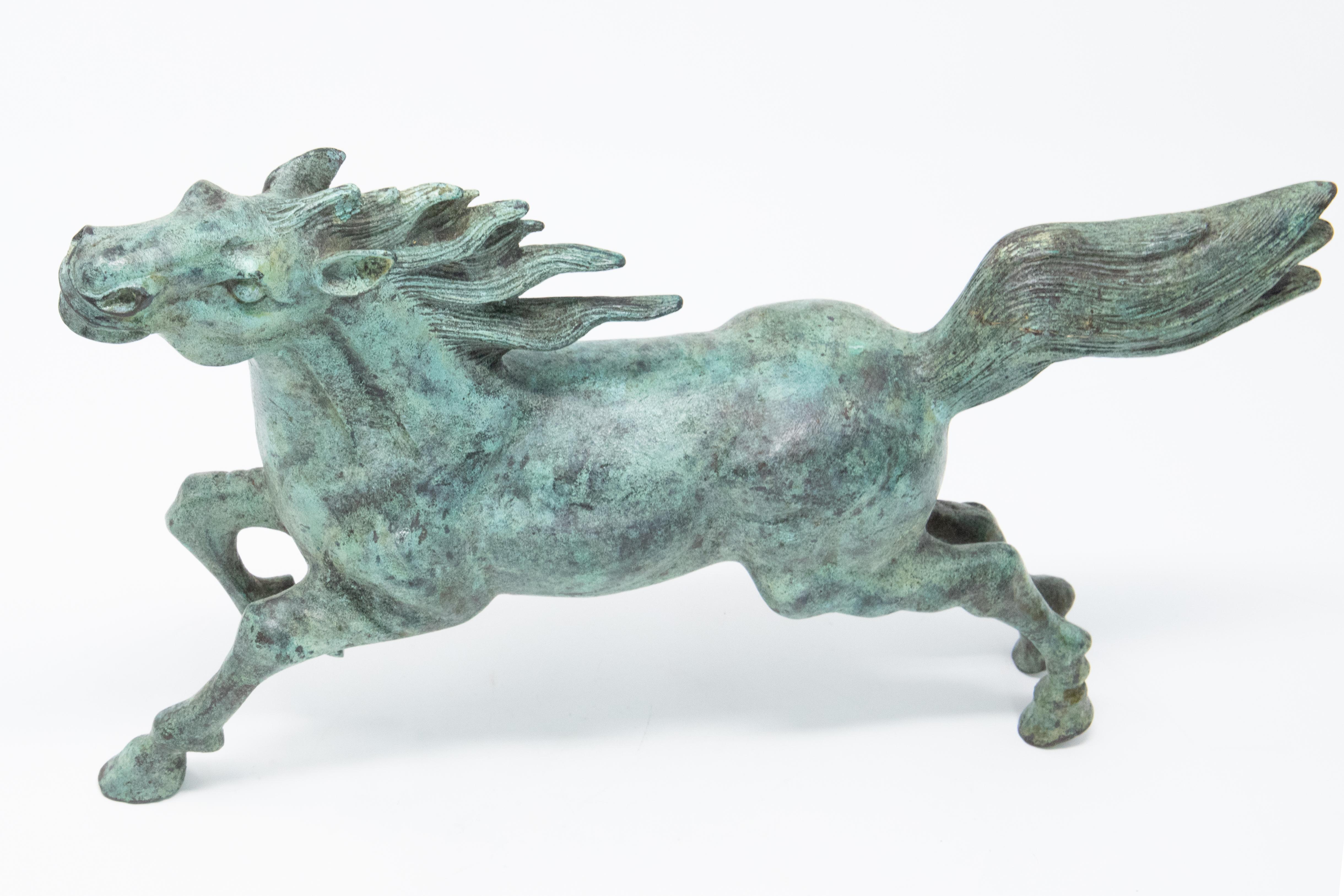 A stunning bronze horse figure showcases a beautiful patina. The figure depicts a horse in the midst of running with its tail and mane flying in the wind. The horse’s head is pointed up in the air and its right front leg is lifted. The piece is