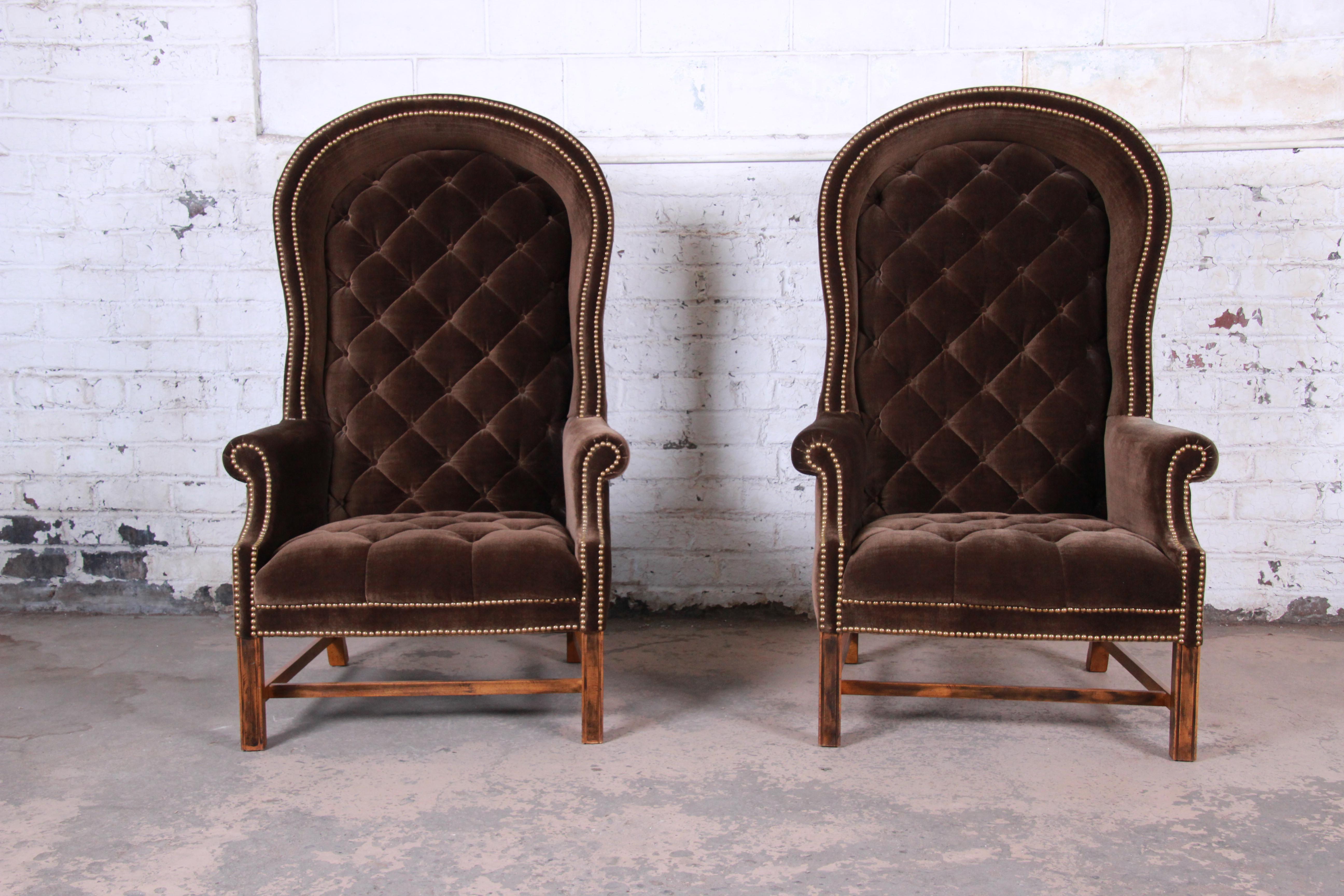 An exceptional pair of midcentury brown velvet hooded canopy Porter's chairs. The chairs feature solid wood legs and frames and gorgeous brass-studded tufted brown velvet upholstery. They are comfortable and ready for use. Very good vintage