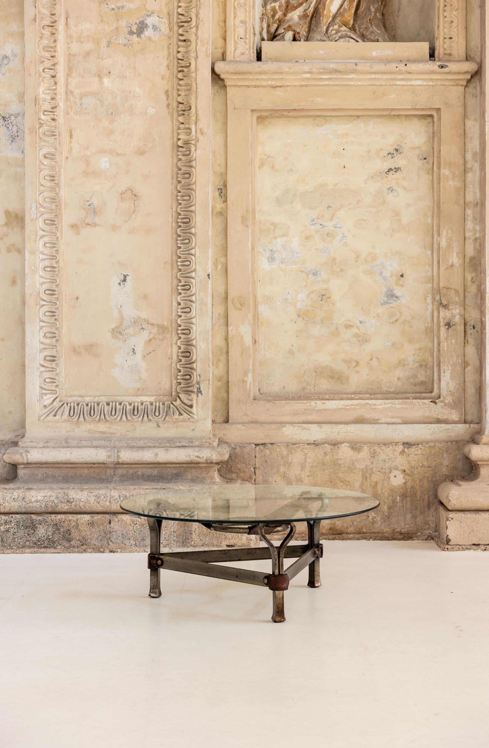 Table basse brutaliste du milieu du siècle par Jean-Pierre Ryckaert. La table est équipée de sangles en cuir épais qui relient de manière unique le trépied et l'anneau central en acier. Un verre rond posé dessus complète la table. Un magnifique