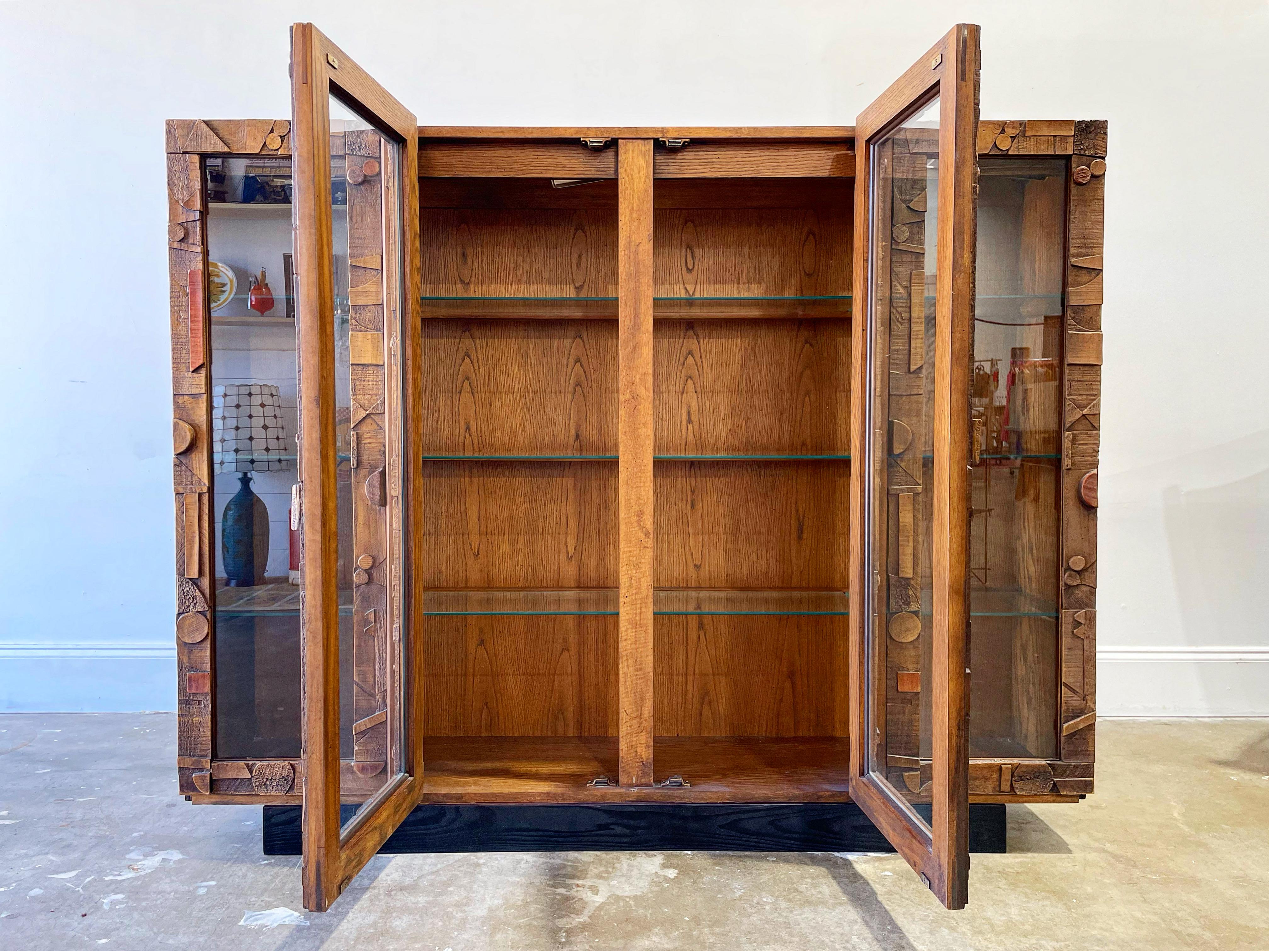 Brutalist style vintage curio display cabinet by Lane. Walnut, resin and glass on an ebonized cypress plinth base. Modern abstract cubist design on the door facades. Glass shelves with interior lighting. Cabinet shows minor signs of use - it is