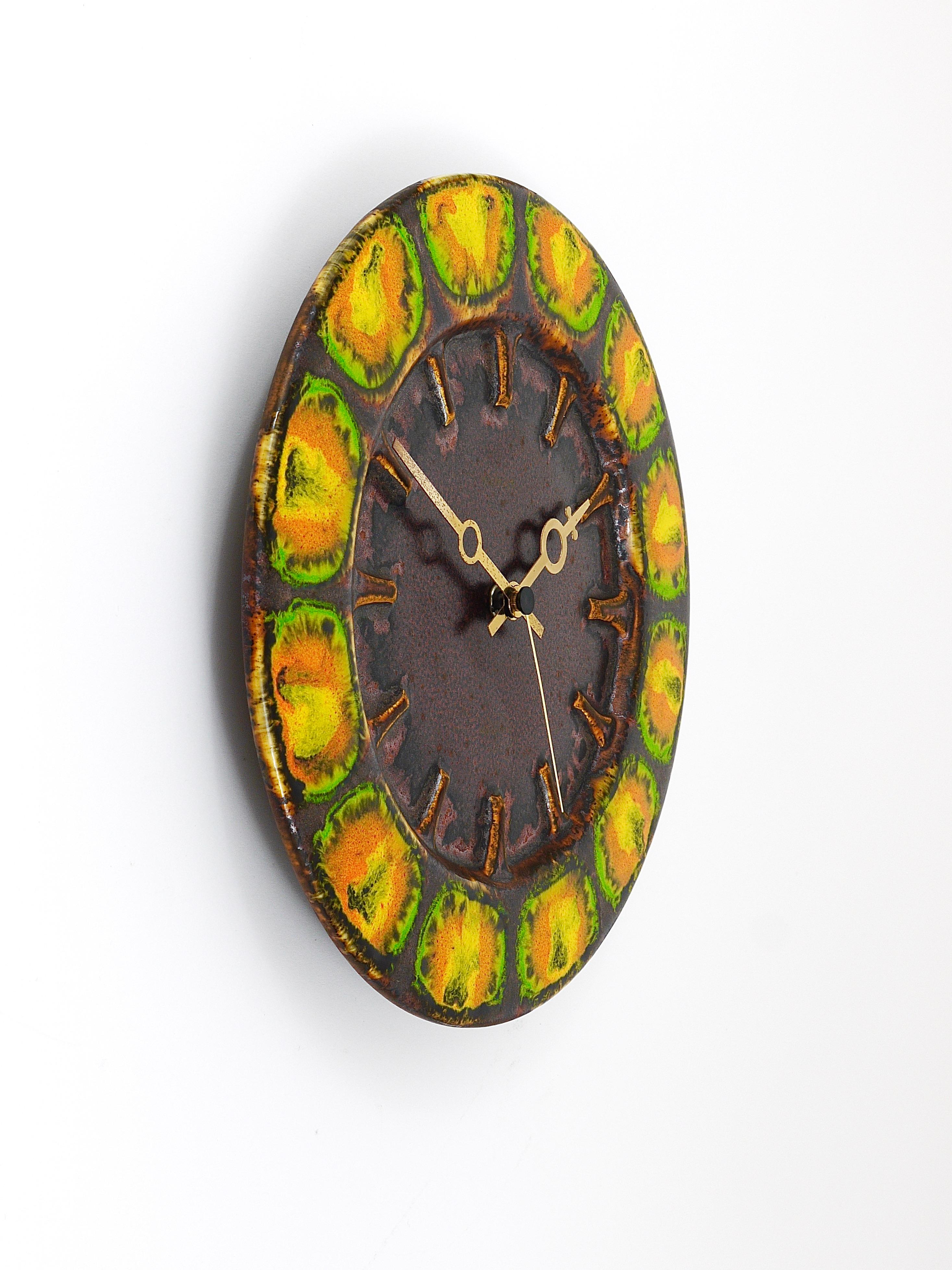 A beautiful round Midcentury Brutalist wall clock, executed by Kienzle Germany in the 1970s. The clock has a housing made of ceramic with a colorful enamel glaze in brown, green, yellow and orange and stylish golden hands. Powered by a standard