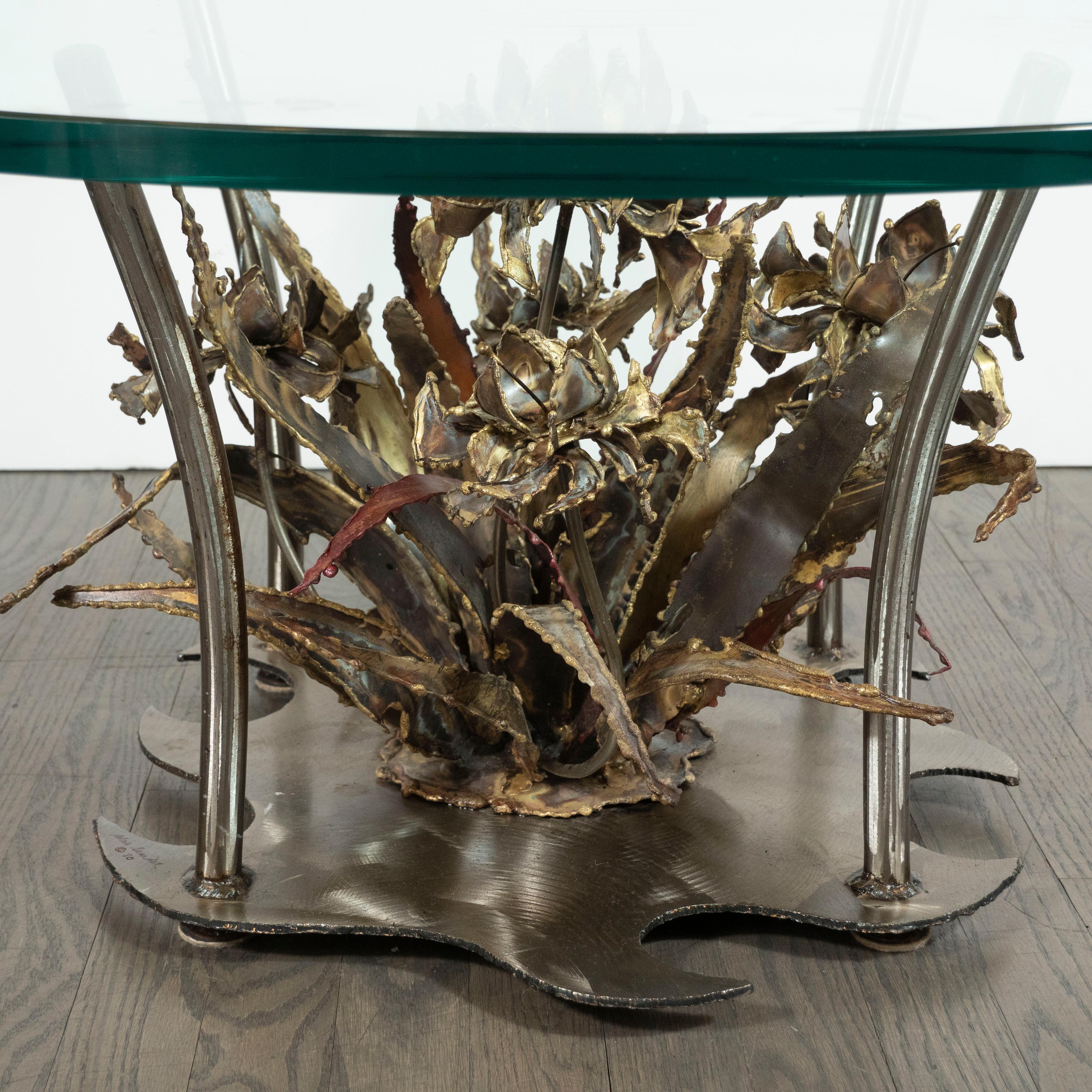 Esta escultural mesa de cóctel fue diseñada por Silas Seandel y fabricada a mano en su estudio de Nueva York, hacia 1980. La mesa tiene una base de acero de forma amorfa, de la que parten cuatro columnas de acero suavemente curvadas. Estas columnas
