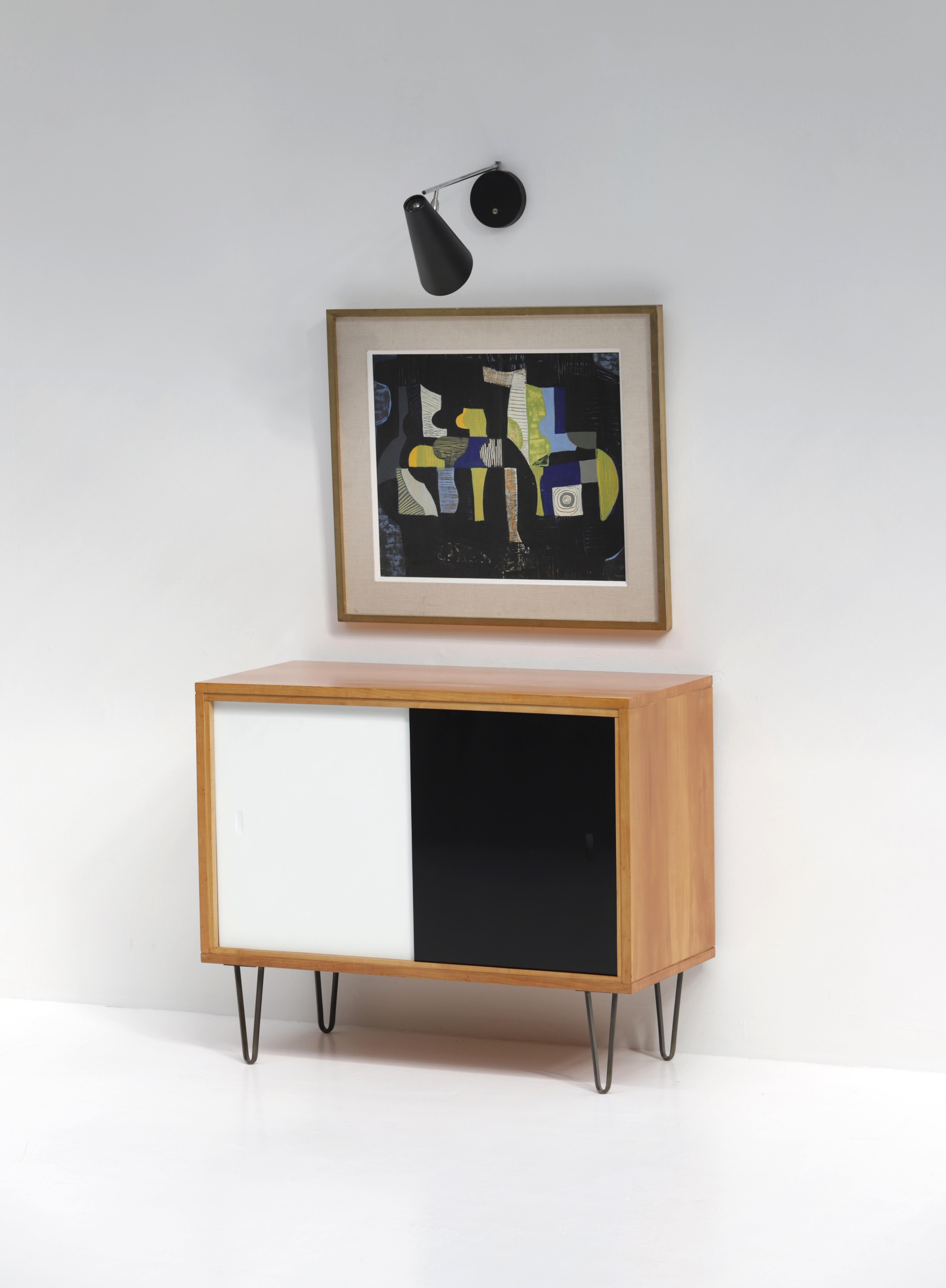 Rare Alfred Hendrickx cabinet with black and white opaline glass sliding doors. It was produced by Belform during the 50s. The hairpin legs combined with the honey colored wood makes it elegant and decorative. The sideboard remains in excellent