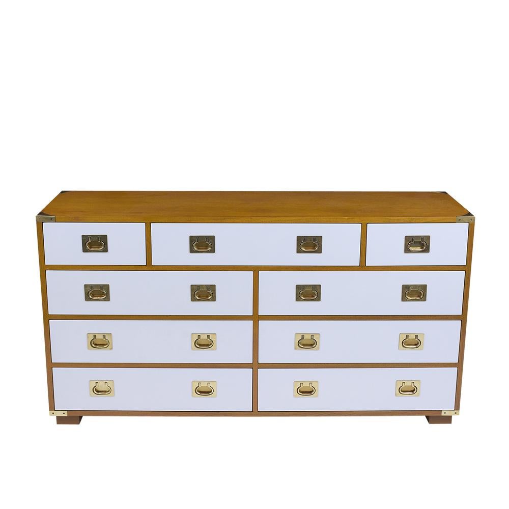 This vintage midcentury campaign nine drawer dresser has been professionally restored is made out of walnut wood, and has been stained in a new maple and white color combination with a lacquered finish. The dresser comes with brass accents on all