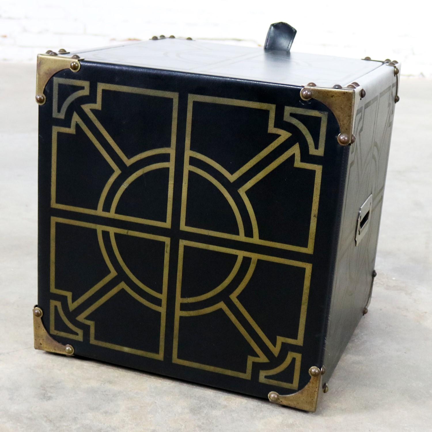 Handsome midcentury Campaign style cube shaped storage ottoman or side table. It is upholstered in black vinyl with gold geometric designs, brass and brass-tone hardware, reversible lid, and its on casters. It is in fabulous vintage condition with