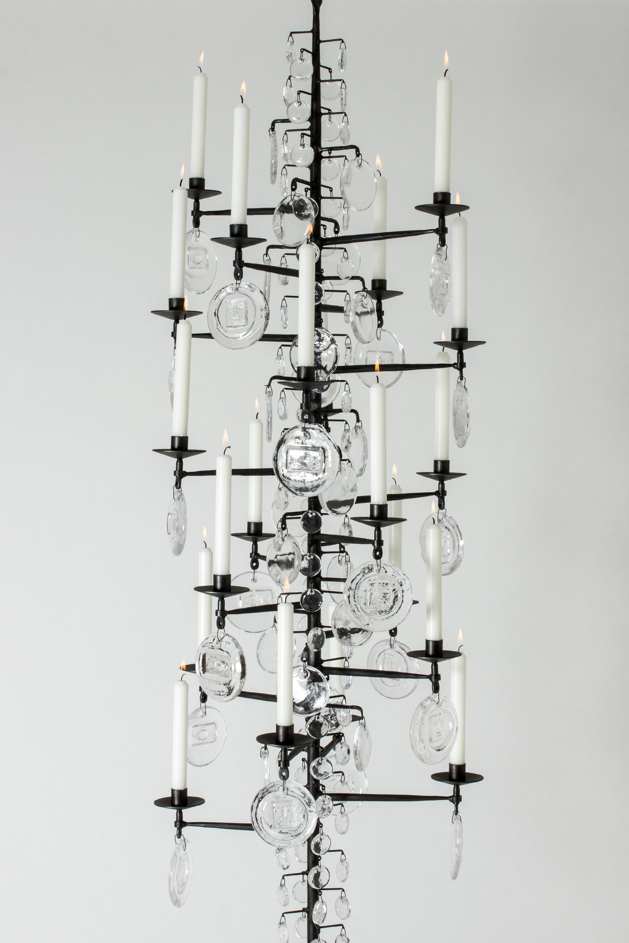 Stunning, oversized candle chandelier by Erik Höglund, made from wrought iron and glass. The long, rustic iron frame is adorned with different sized glass medallions that look like large rain drops on a bare tree. The biggest medallions are embossed