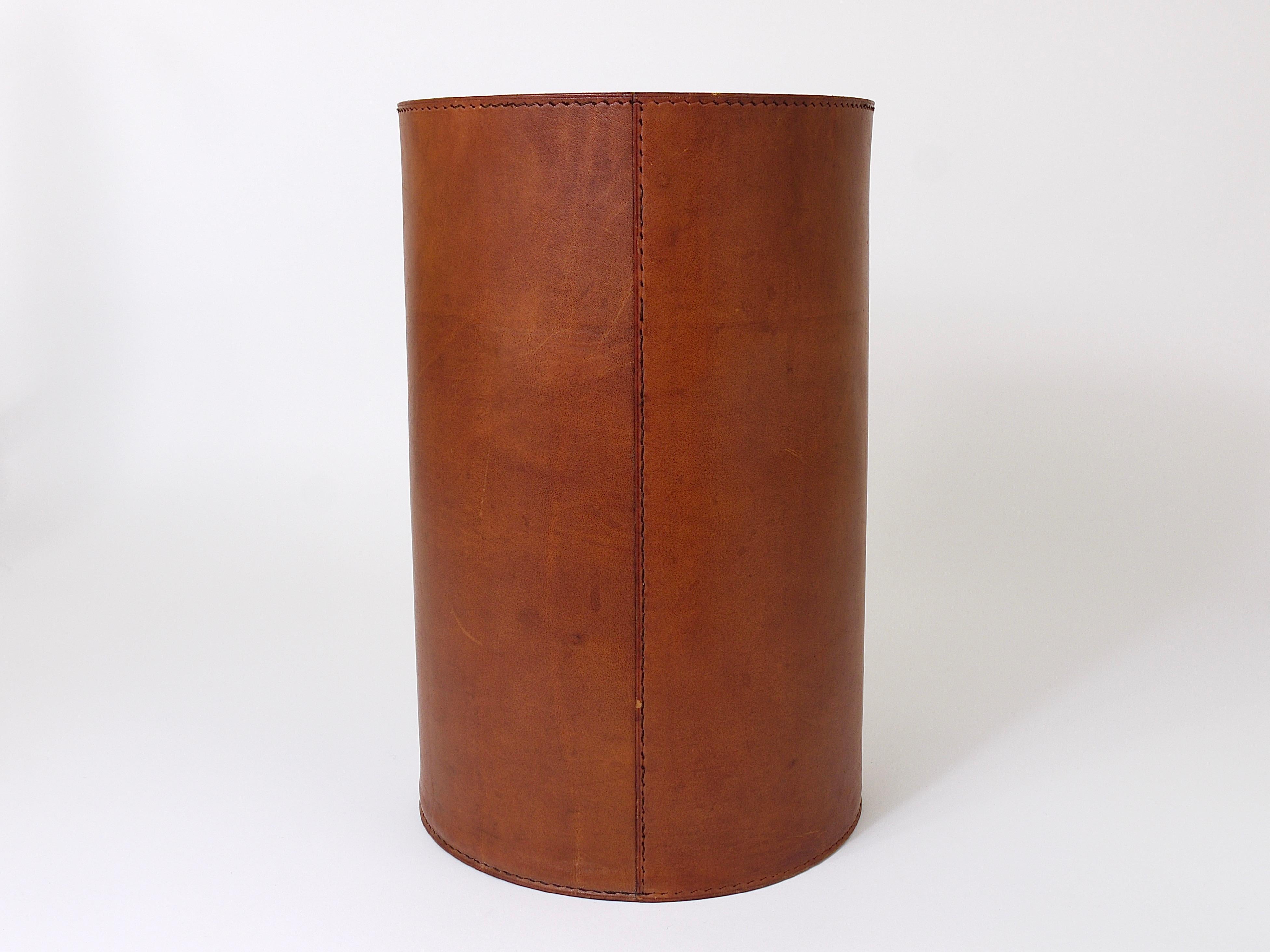 A beautiful cylindric Mid-Century Modern wastepaper basket from the 1950s, designed an executed by Carl Auböck, Vienna. Made of cognac brown leather. The basket is showing signs of age and the leather charming patina.