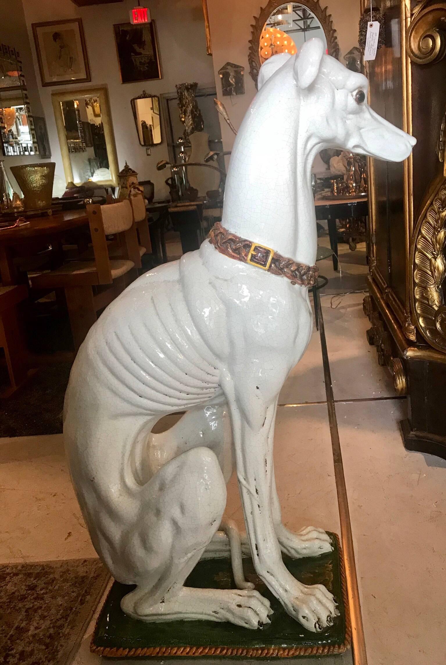A lifesize, very detailed, ceramic sculpture of a whippet or greyhound dog seated on a green cushion with bronze colored trim and a dog collar. Made in Italy, circa 1950s.