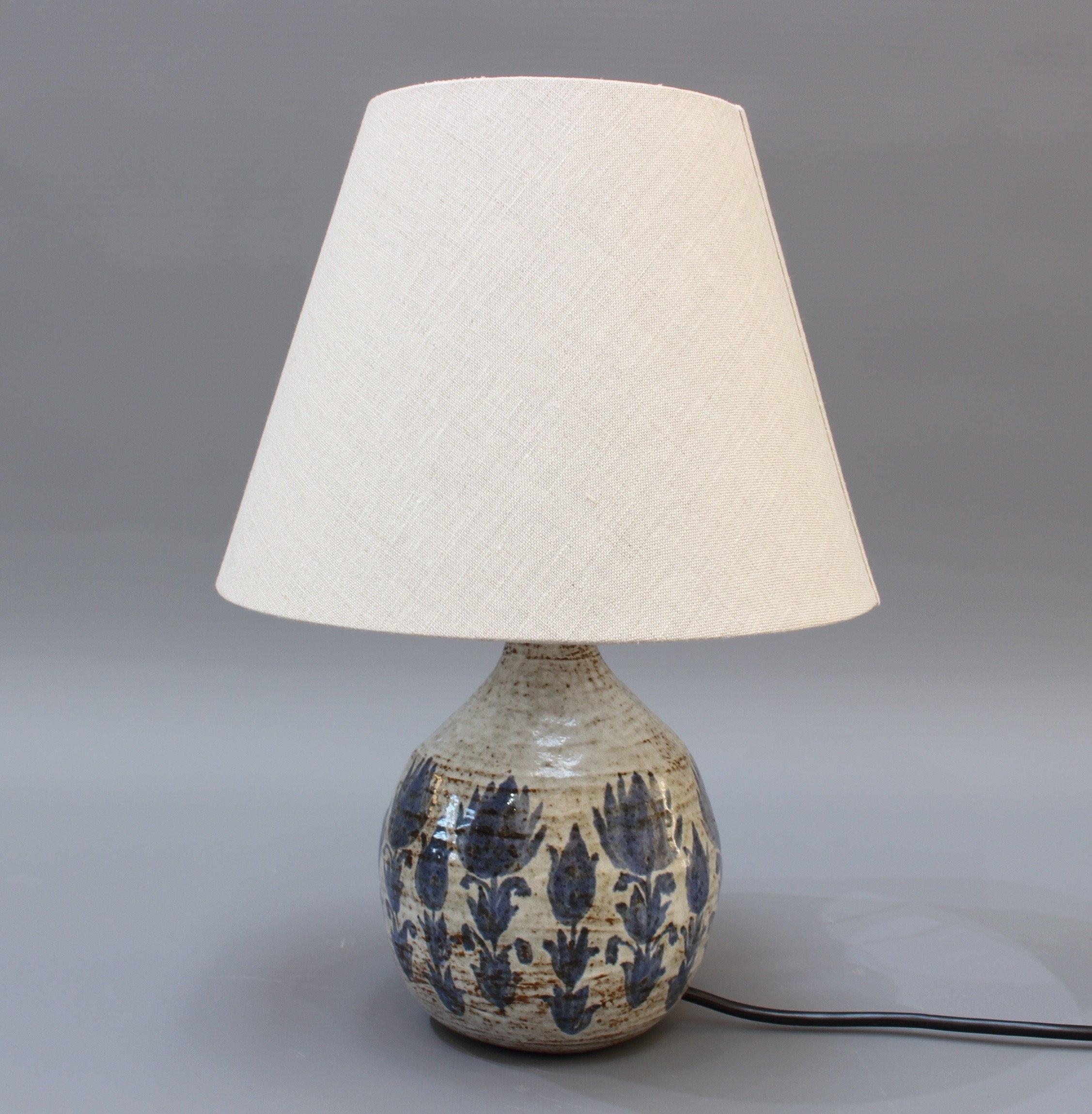 Midcentury ceramic lamp with blue flower motif (circa 1960s). A chalk-white base glaze with scattered brown speckles and lines is covered with hand painted blue flowers over this diminutive, charming flask-shaped table lamp. In good vintage