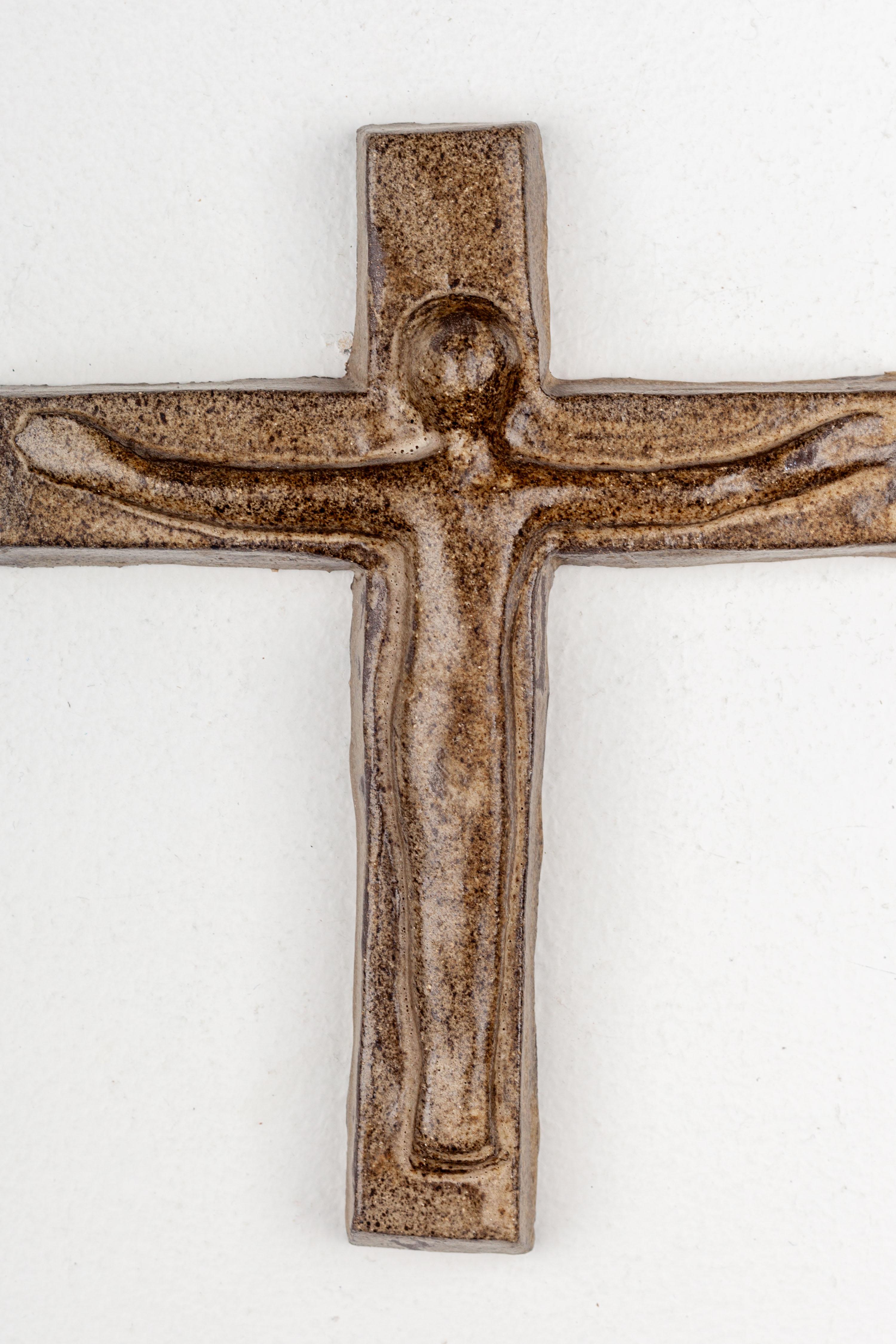 This midcentury ceramic wall cross, created in a European Pottery Studio, features an uncomplicated design. The Christ silhouette relief on the cross is hand-painted, showcasing a glossy point texture with earthy colors resembling granite. It