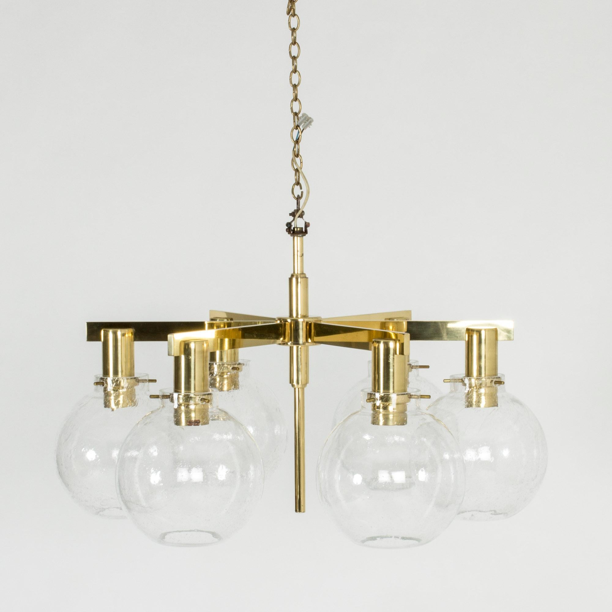 Beautiful brass and glass chandelier by Hans-Agne Jakobsson. Clear glass shades with bubbles in the glass, suspended with brass pins. The body of the chandelier hangs from a brass chain.