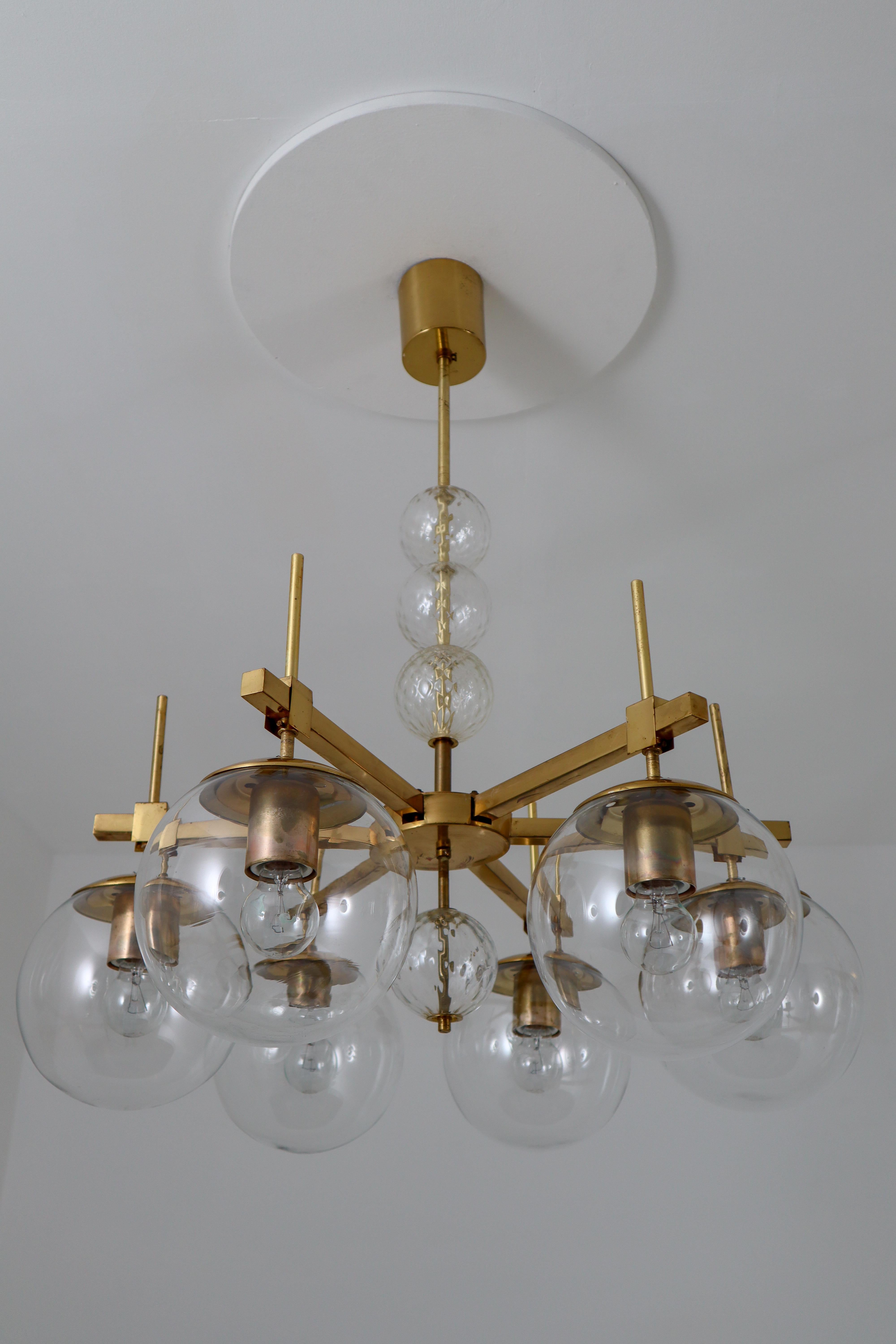 Set of three brass chandeliers was produced in Europe in the 1960s. A spirited and chic design set chandeliers with brass fixture and hand blown glass. The chandelier with brass frame consist of six lights, formed in a circle, with glass shades. The