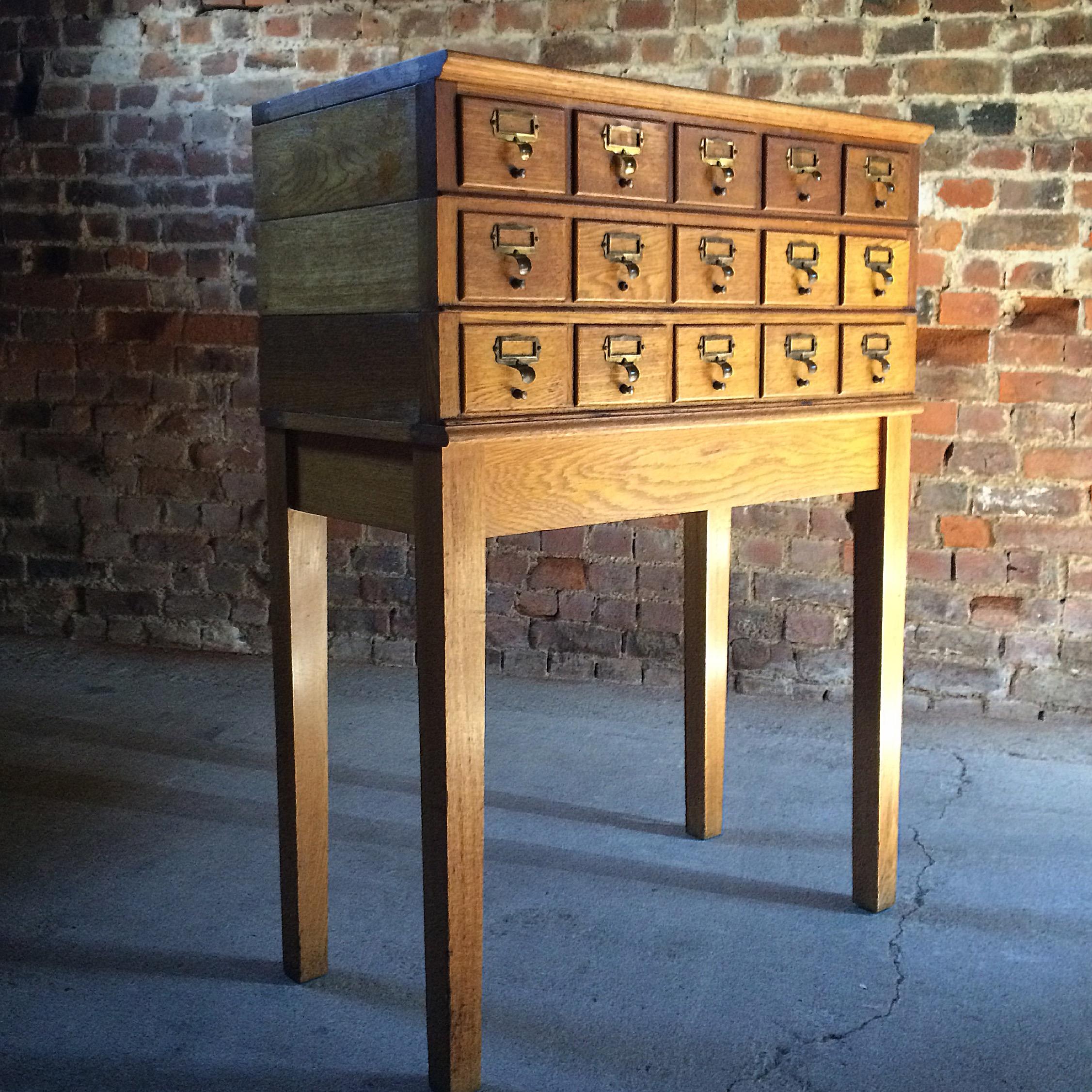 A magnificent mid-20th century haberdashery industrial oak stacking office chest cabinet, having a bank of 15 drawers each with brass index card holder, raised on a base with square section supports, the eleven drawer sections each stack on top of