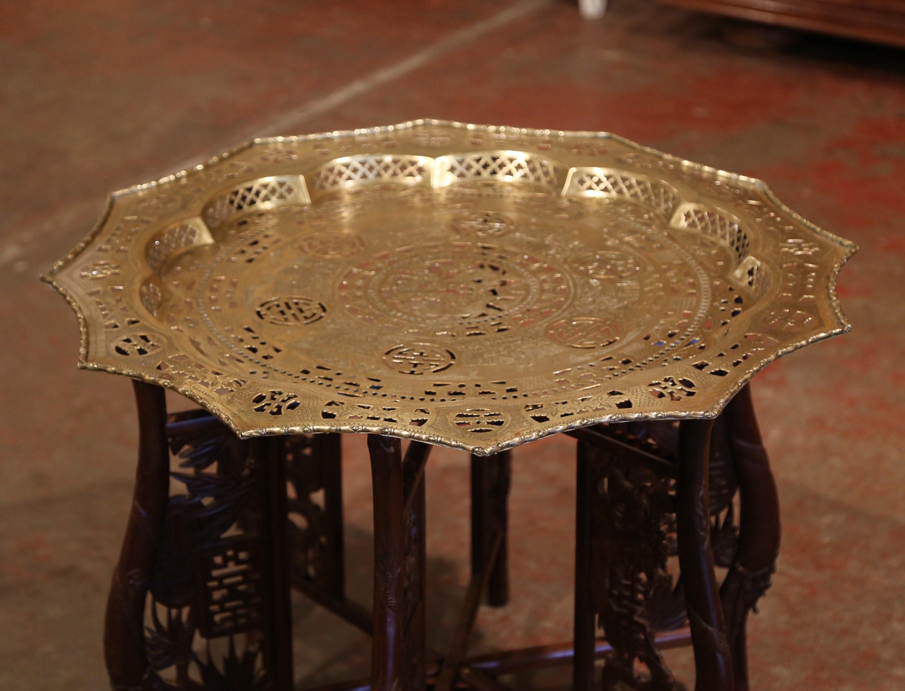 This small, versatile coffee table was crafted in China, circa 1950. The folding base with decorative supports has six carved legs which can easily be folded up flat. The brass tray plateau decorated with engraved geometric motifs has a twelve sided