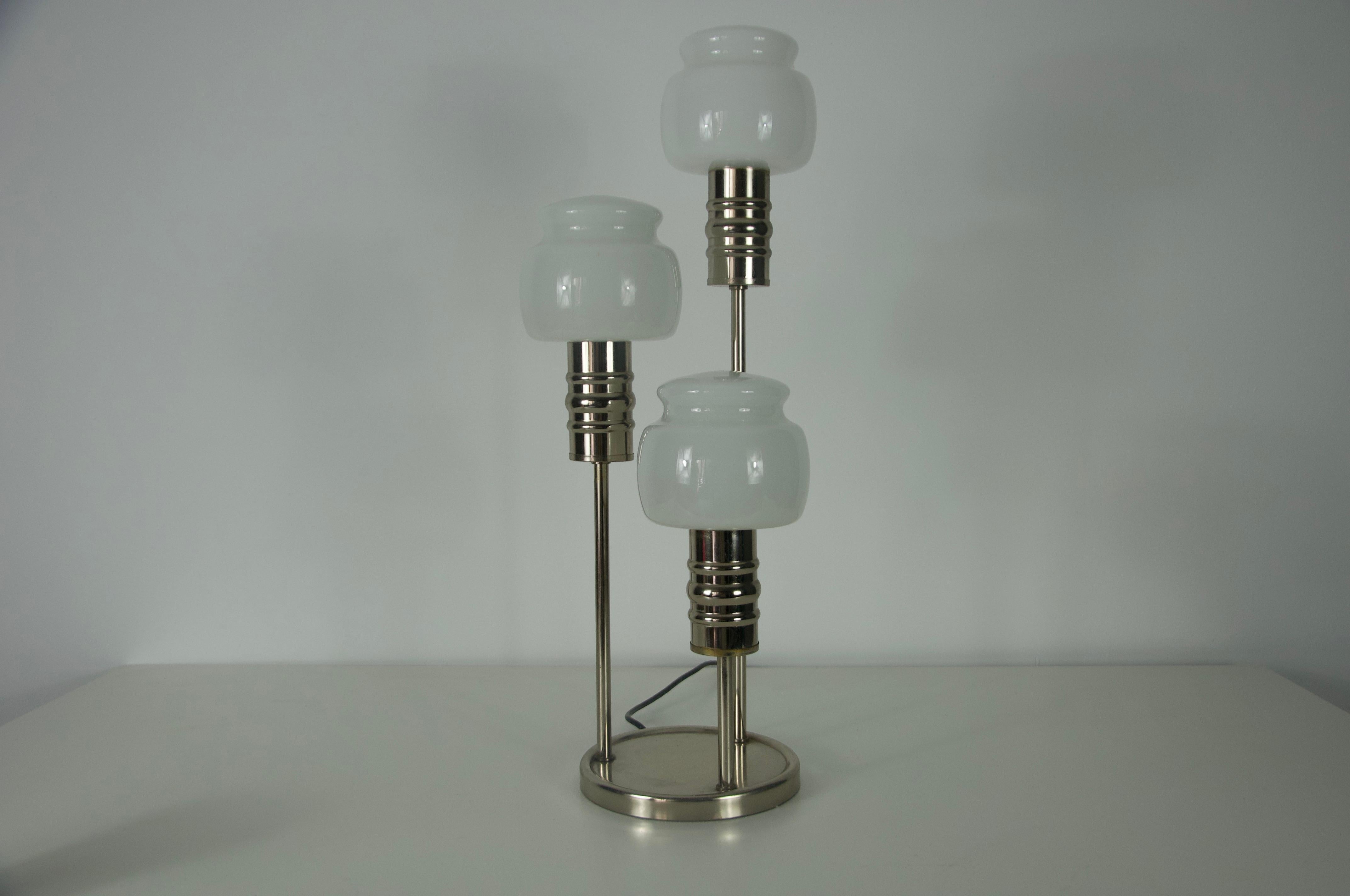 Cette élégante lampe de table allemande des années 1960 est un bel exemple de design du milieu du siècle, alliant fonctionnalité et esthétique raffinée. Fabriquée avec un cadre en chrome poli et ornée de trois abat-jours en verre opale doucement
