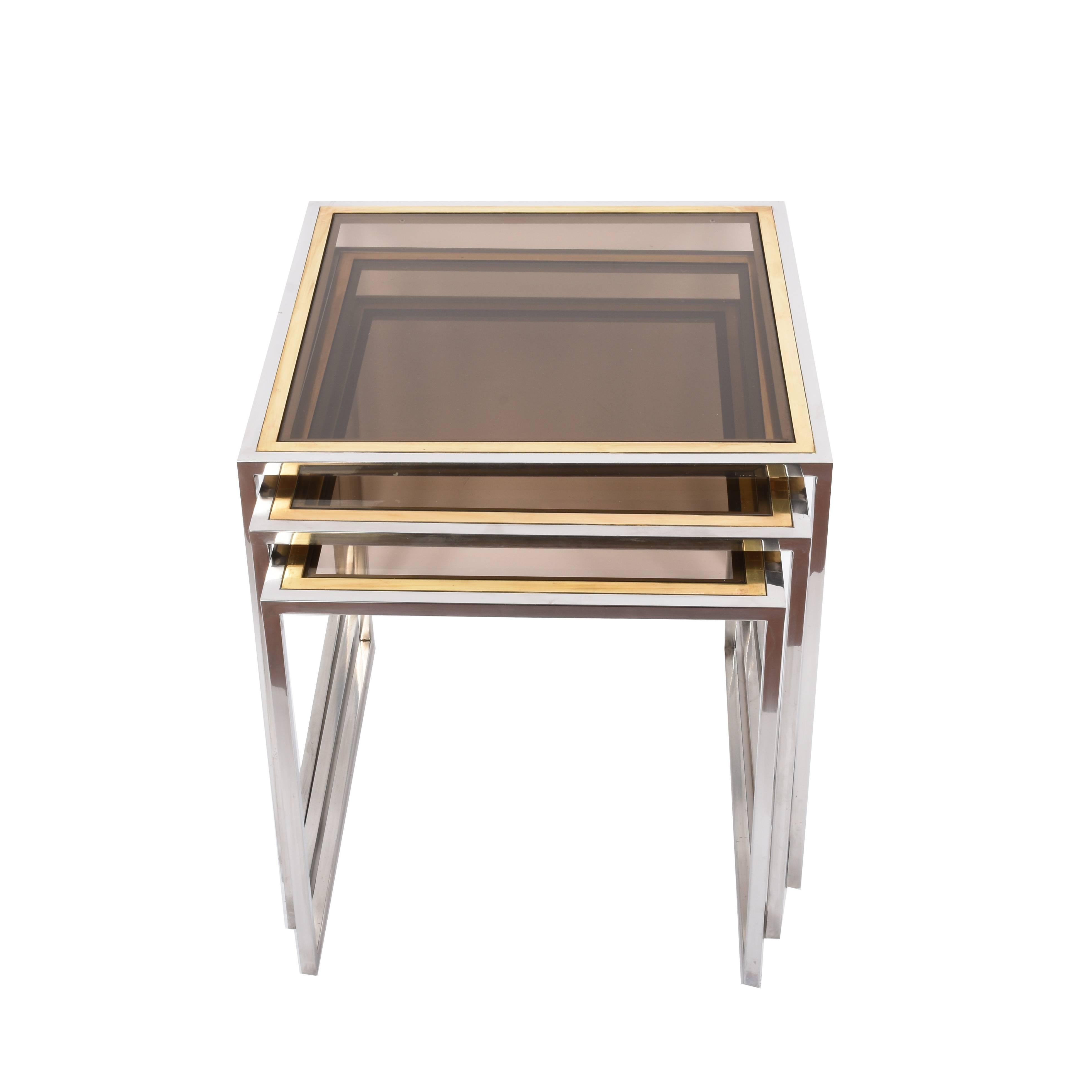 Wonderful set of three nesting tables in chromed metal, brass and smoked glass.

These Mid-Century Modern amazing tables were produced in Italy during the 1970s. 

This set, both elegant and functional, is perfect for a midcentury living