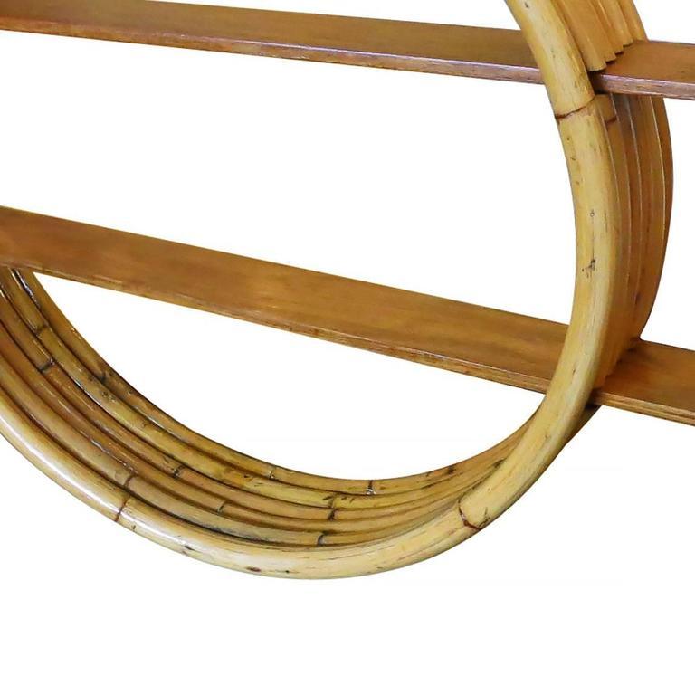 Circular rattan wall self, circa 1950. This rare rattan wall shelf features unique five strand stack rattan frame made with cut-out sections which hold two mahogany shelves.

Restored to new for you.

All rattan, bamboo and wicker furniture has been