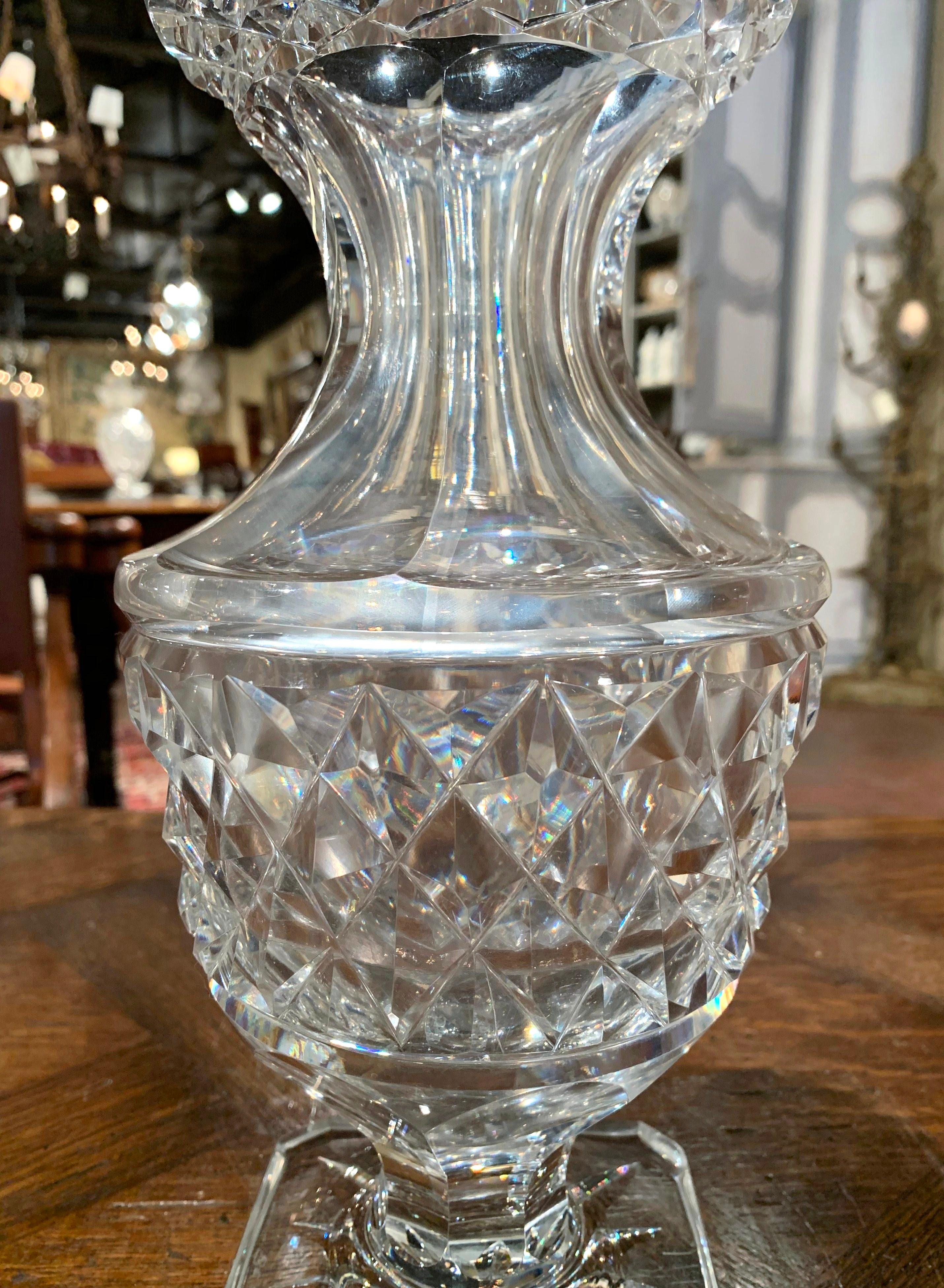 Decorate a console table or buffet with this elegant glass vase. Crafted in France circa 1970, the luxurious cut glass vessel stands on a square base, is shaped as a neoclassical urn with a wide mouth at the top, and is decorated throughout with