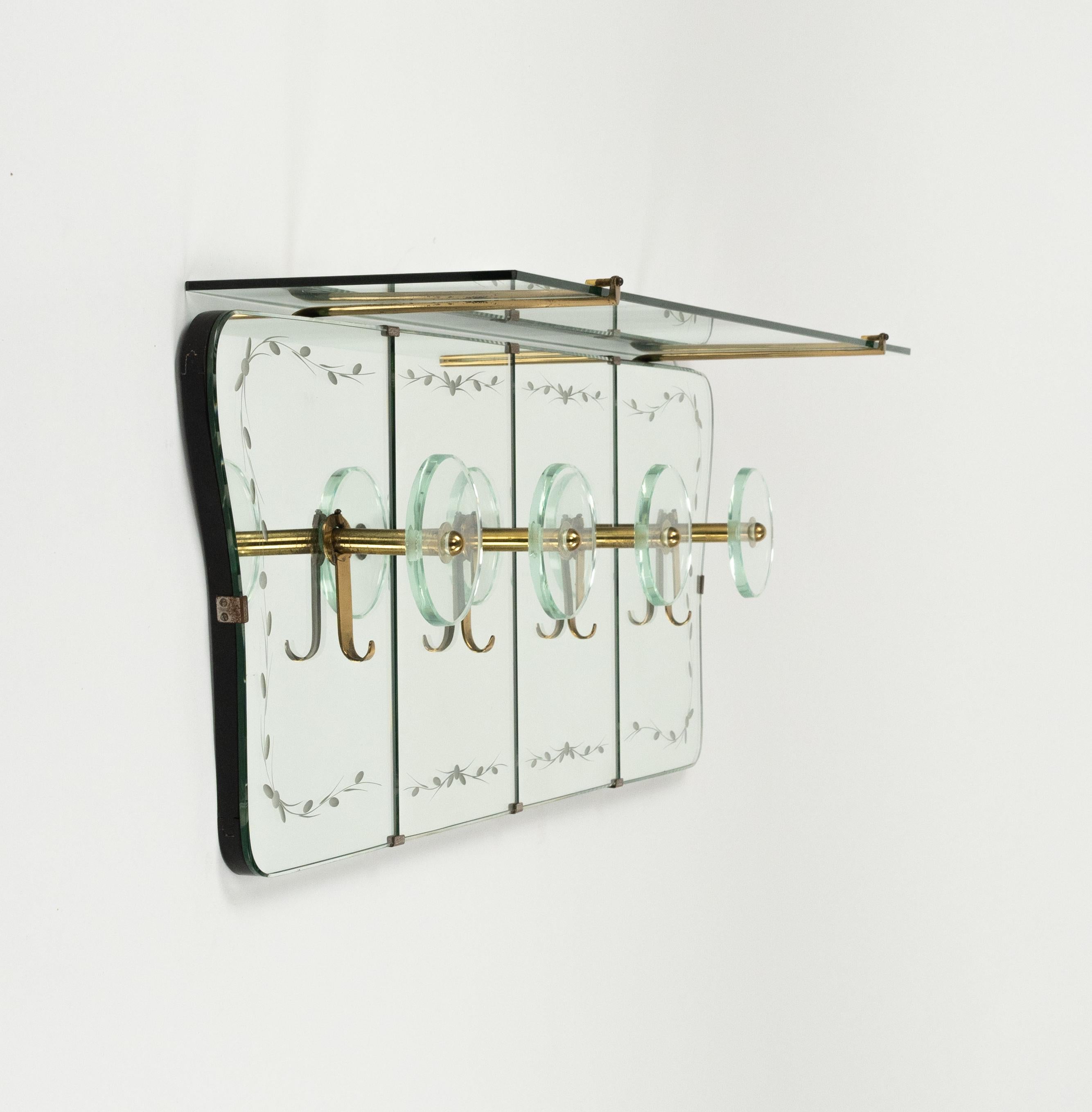Stupefacente appendiabiti da parete a specchio del Medioevo con struttura a ripiano superiore in vetro con eleganti dettagli intagliati e quattro ganci circolari in vetro e ottone di Cristal Arte.   

Prodotto in Italia negli anni '50.