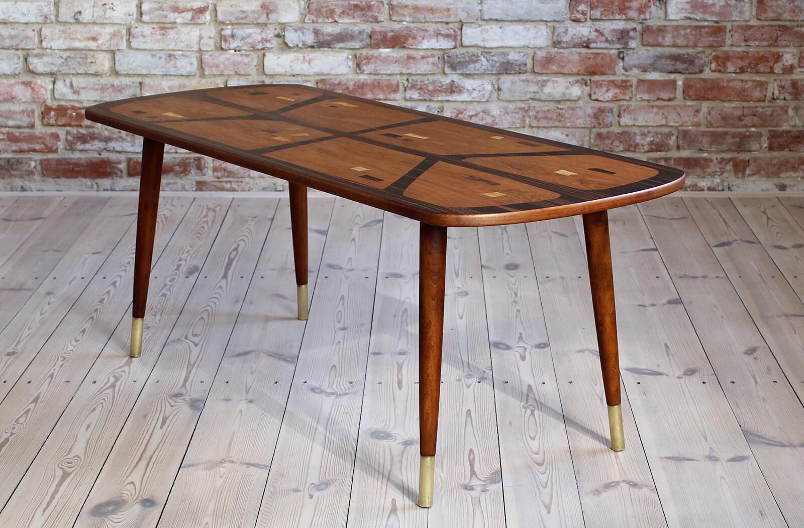 This beautiful coffee table was most probably made circa 1960s. It features 4 slender legs, all finished with brass, which was a very characteristic element of furniture in those years. The magnificent table top is veneered with different wood
