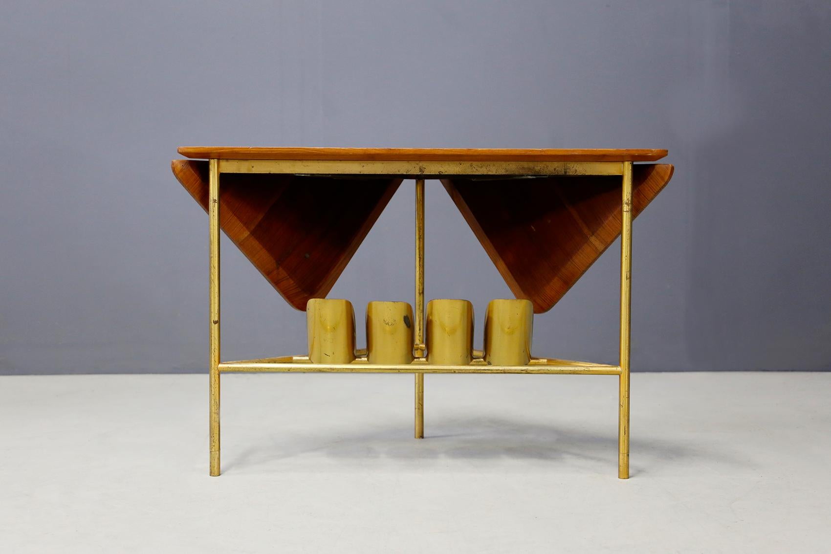 Folding coffee table attributed to Ignazio Gardella from 1950. The coffee table is made of brass for its structure and wooden shelves. The peculiarity of the cabinet is in its brass bottle holders placed in the lower compartment. Its wooden shelf is