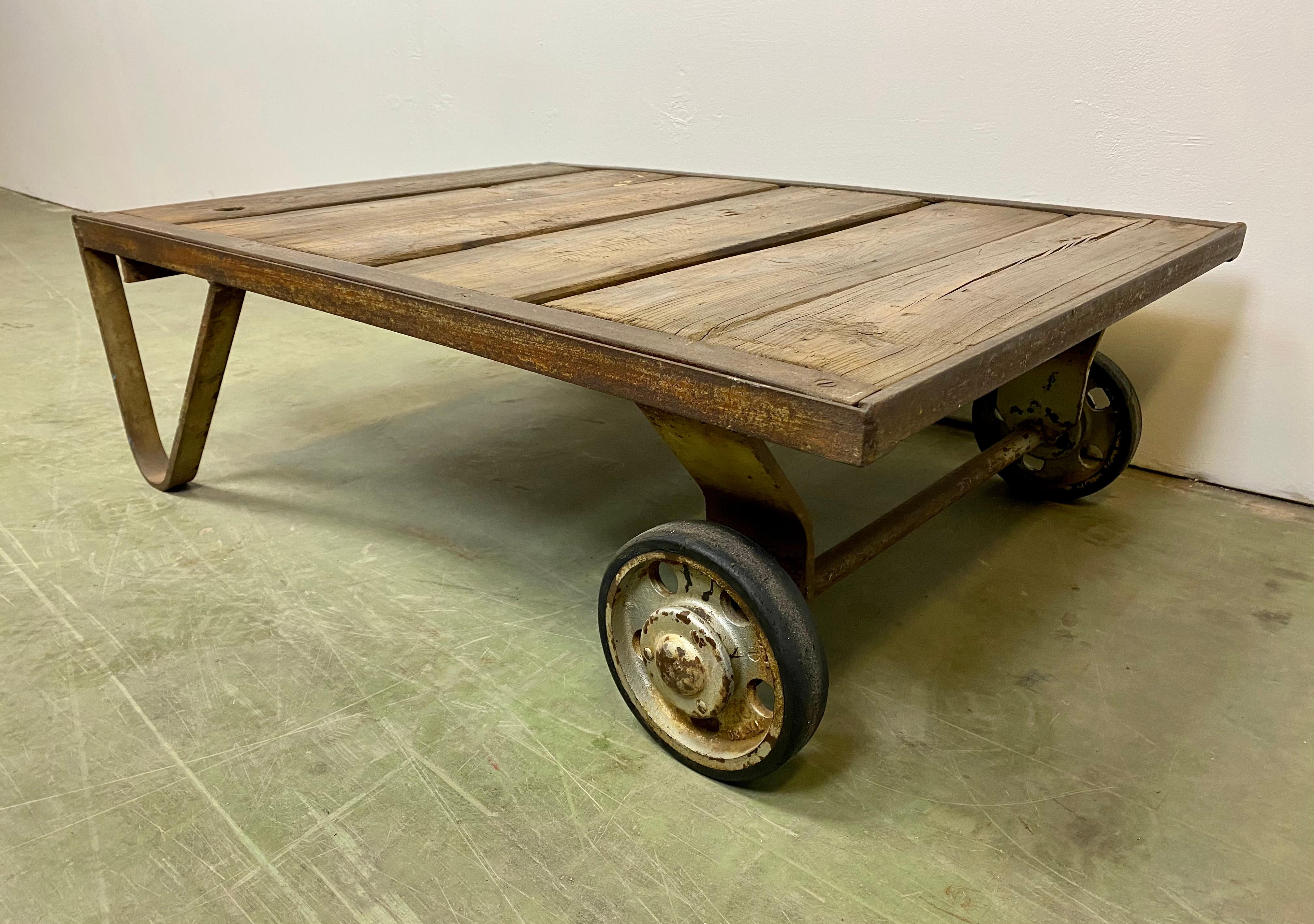 Former pallet truck from a factory now serves as a coffee table. It features a iron construction with two wheels and a solid wooden plate. The weight of the table is 35 kg.