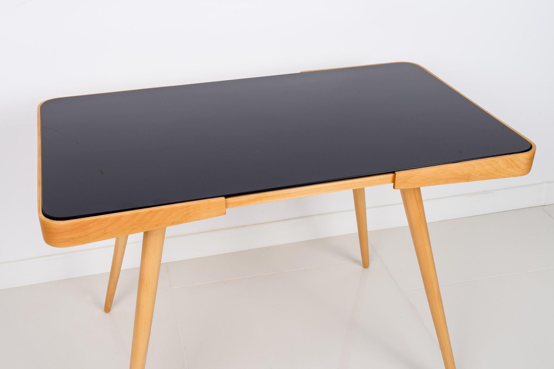 This beautiful coffee table was made in the 1960s, designed by famous Czech designer - Jiri Jiroutek. It was awarded at the Expo fair in 1958 in Brussels. It features 4 slender legs and top made of beech wood, covered with black glass. The piece is