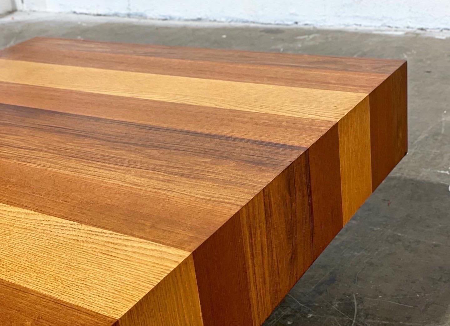 Stellar square mixed wood cocktail by Dyrlund. Designed and built in Denmark circa 1973. Table rests on a recessed black plinth base. Top consists of mixed veneers of walnut, teak, rosewood, oak, palisander, and butternut. Visually stunning - the